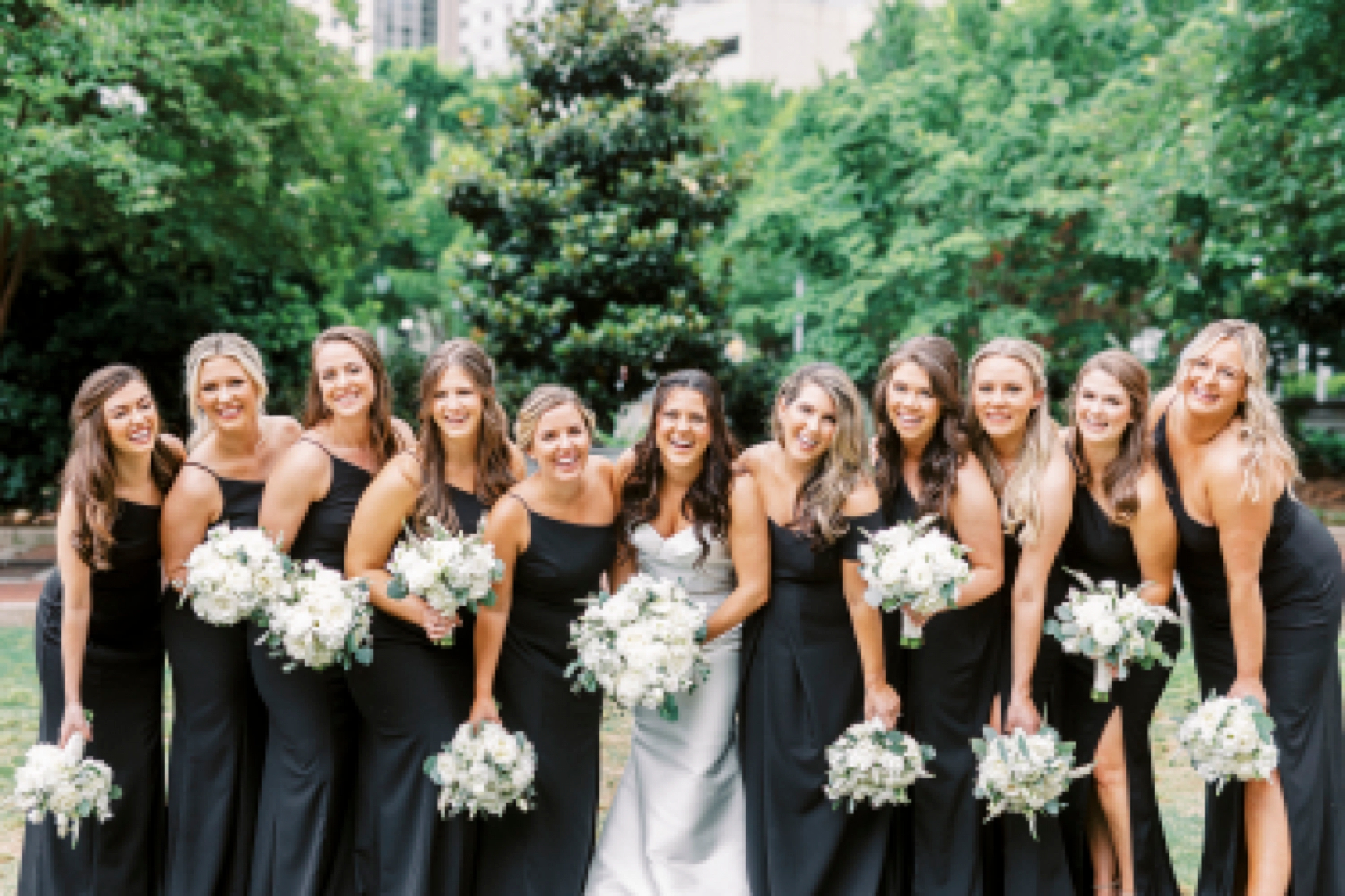 bride stands with bridesmaids in black gowns with ivory bouquets