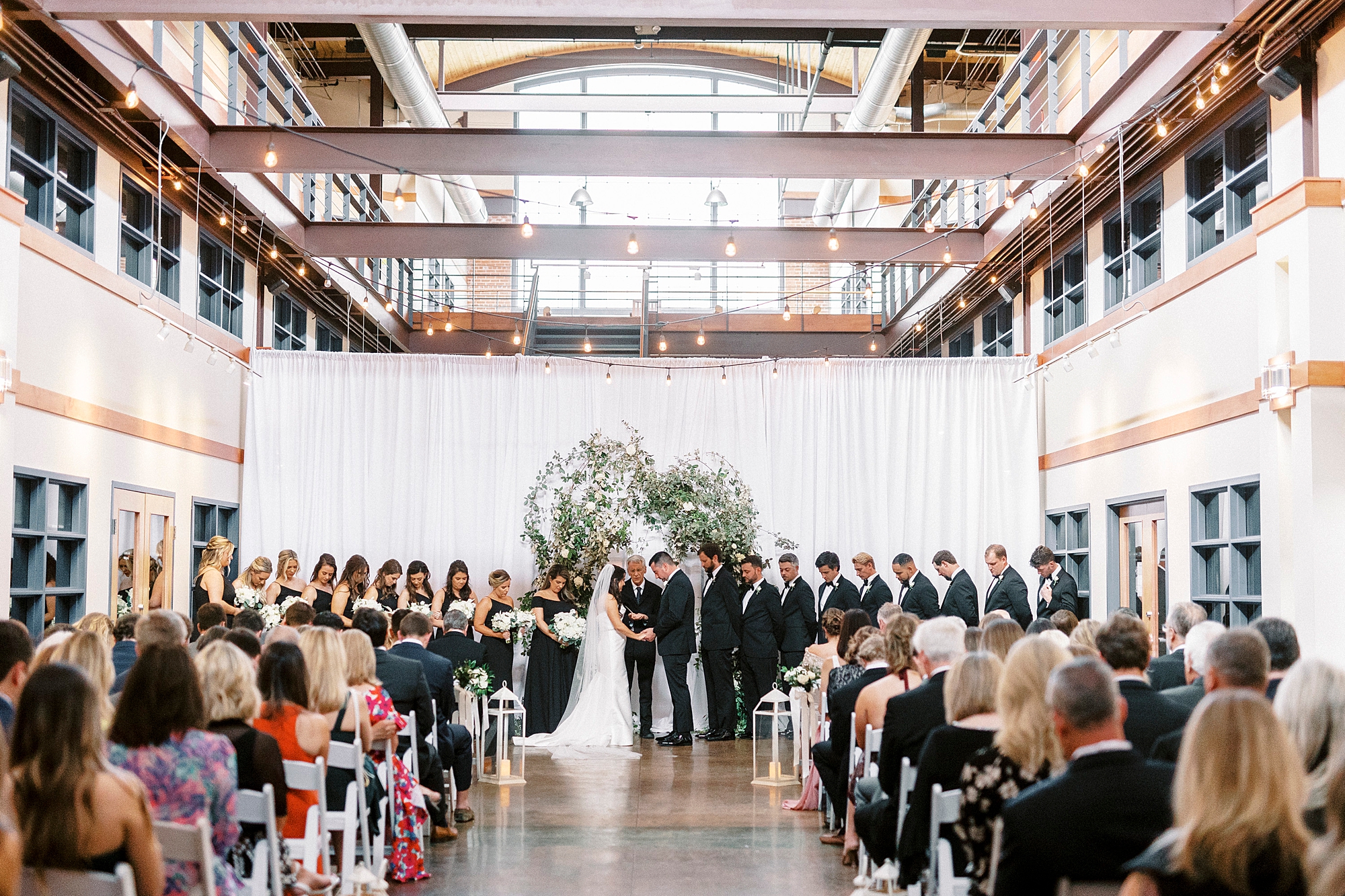 Design Atrium wedding ceremony for couple with wedding party in all black attire