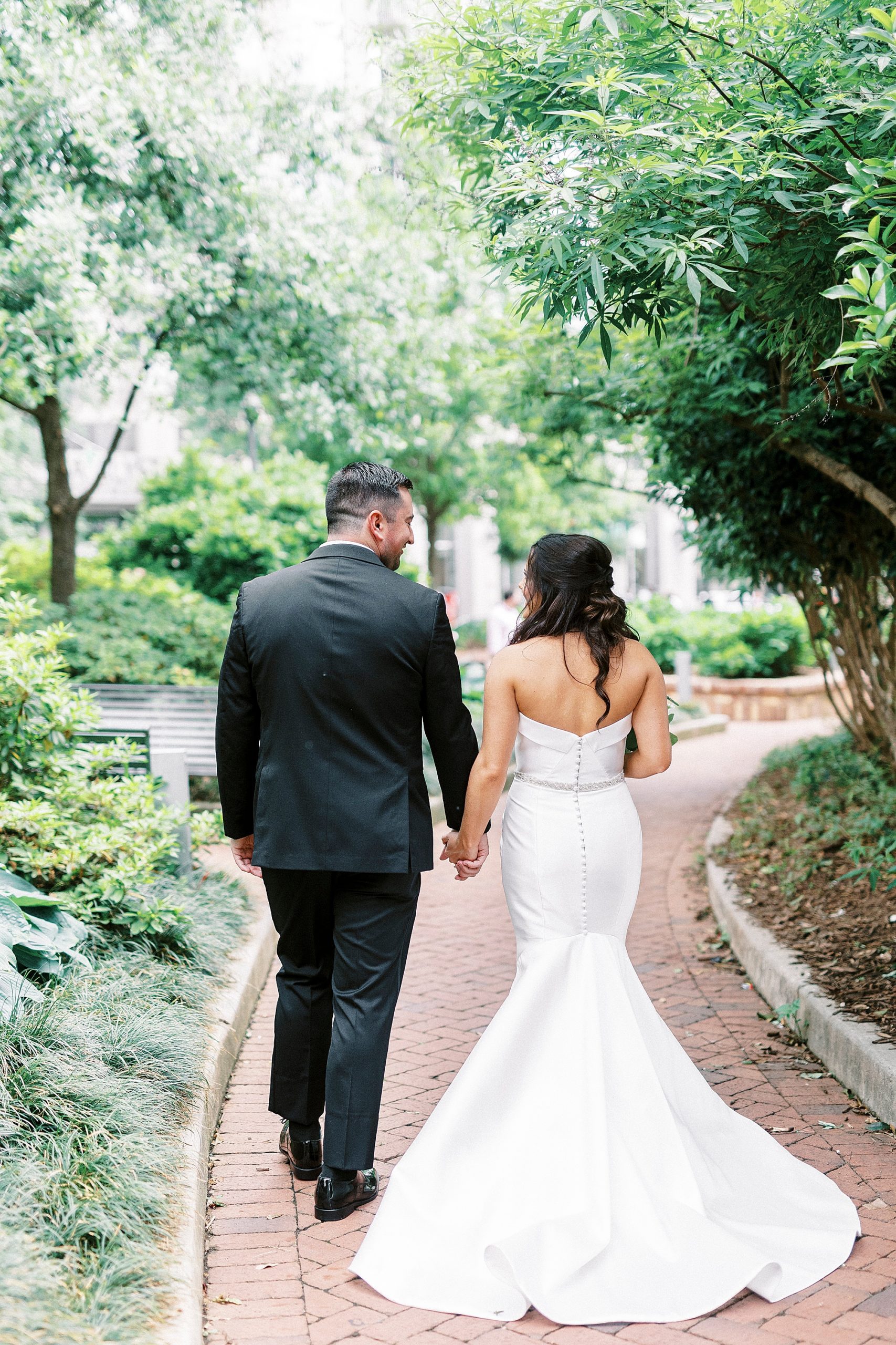 newlyweds hold hands walking down Charlotte NC park pathway