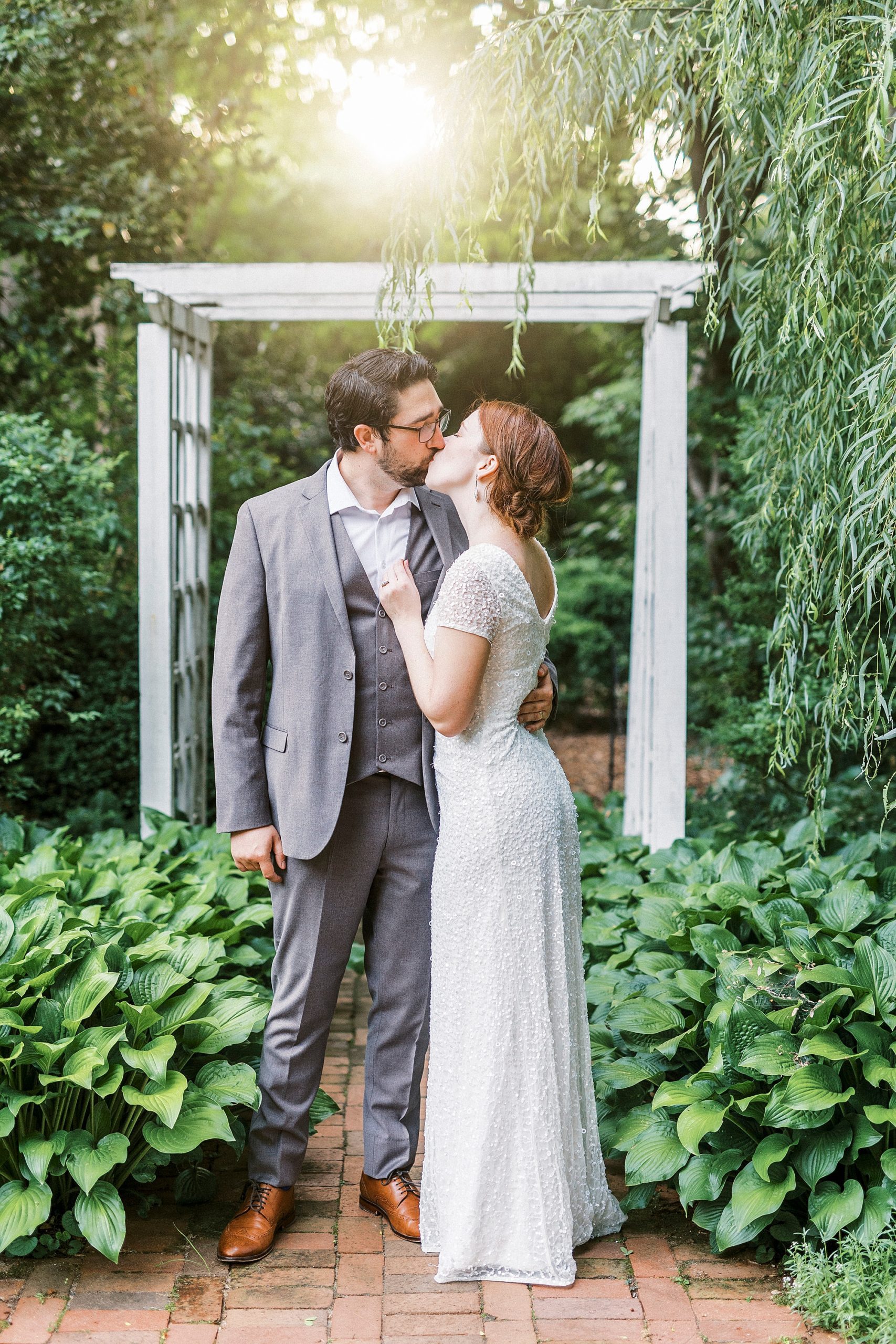 woman kisses man near white arbor in gardens