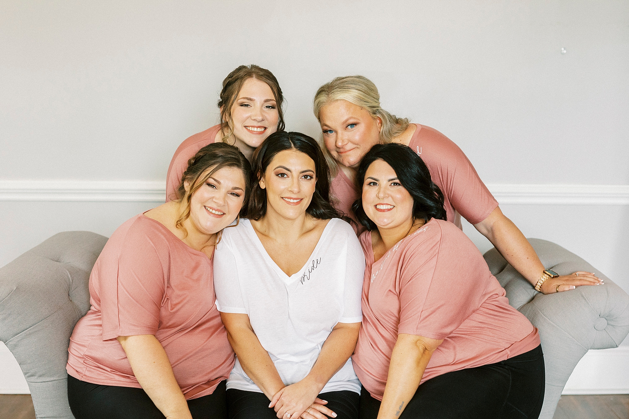 bride sits with bridesmaids in pink robes 