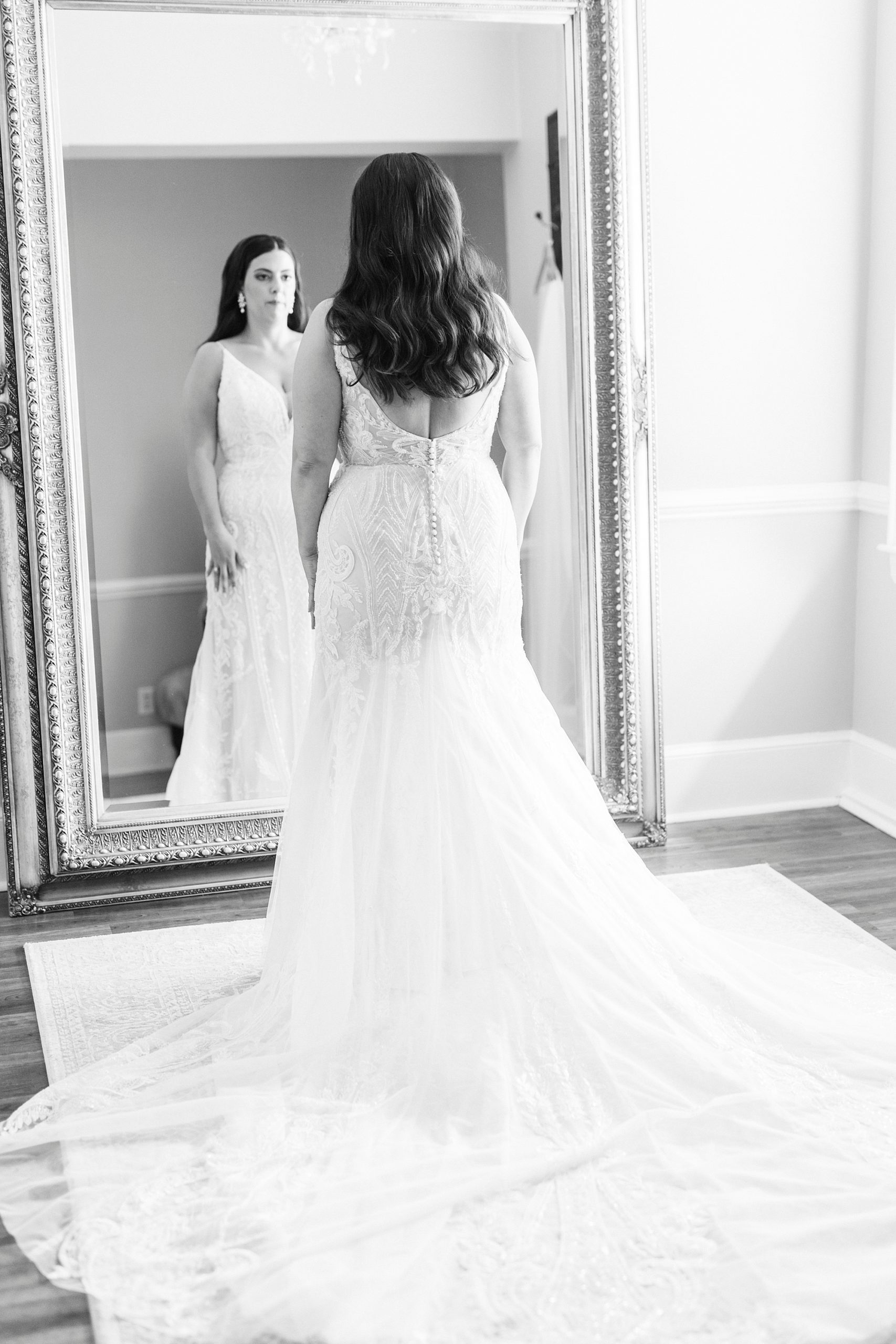 bride stands looking in mirror with dress train behind her