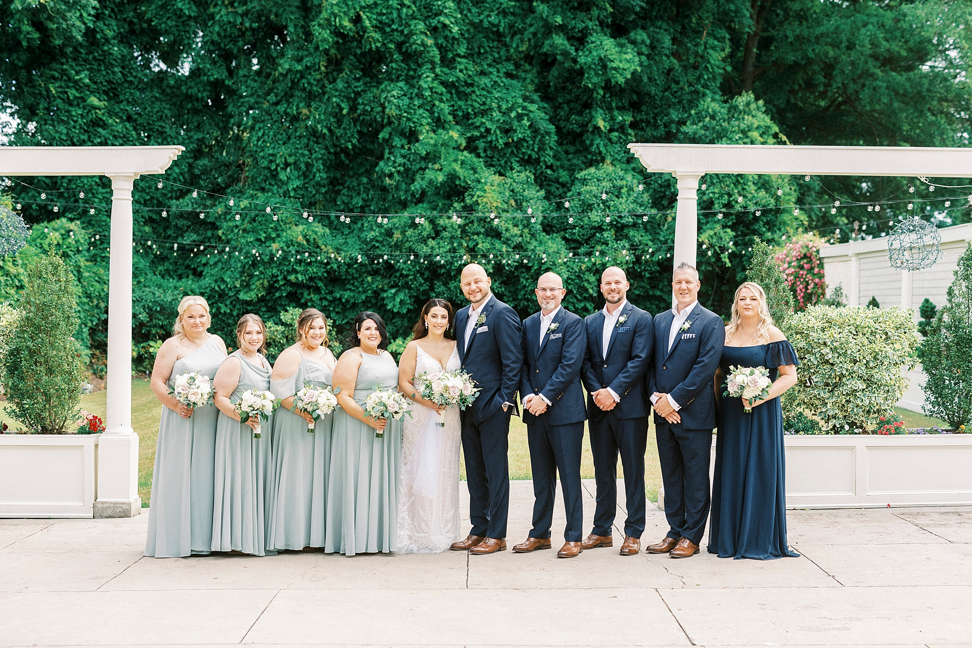 bride and groom stand with wedding party in light green dresses and navy suits