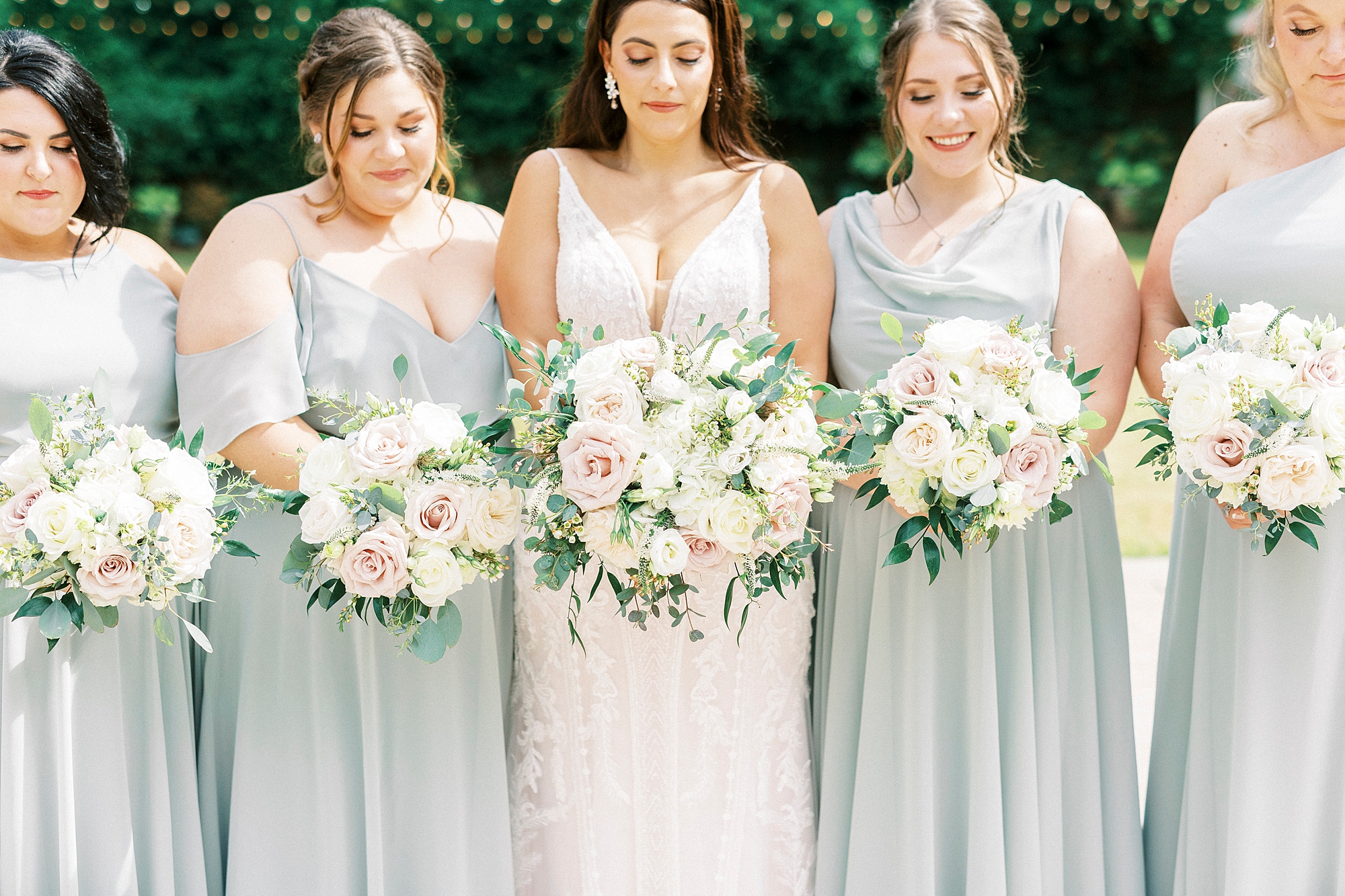 bride and bridesmaids hold bouquets of white and pink roses