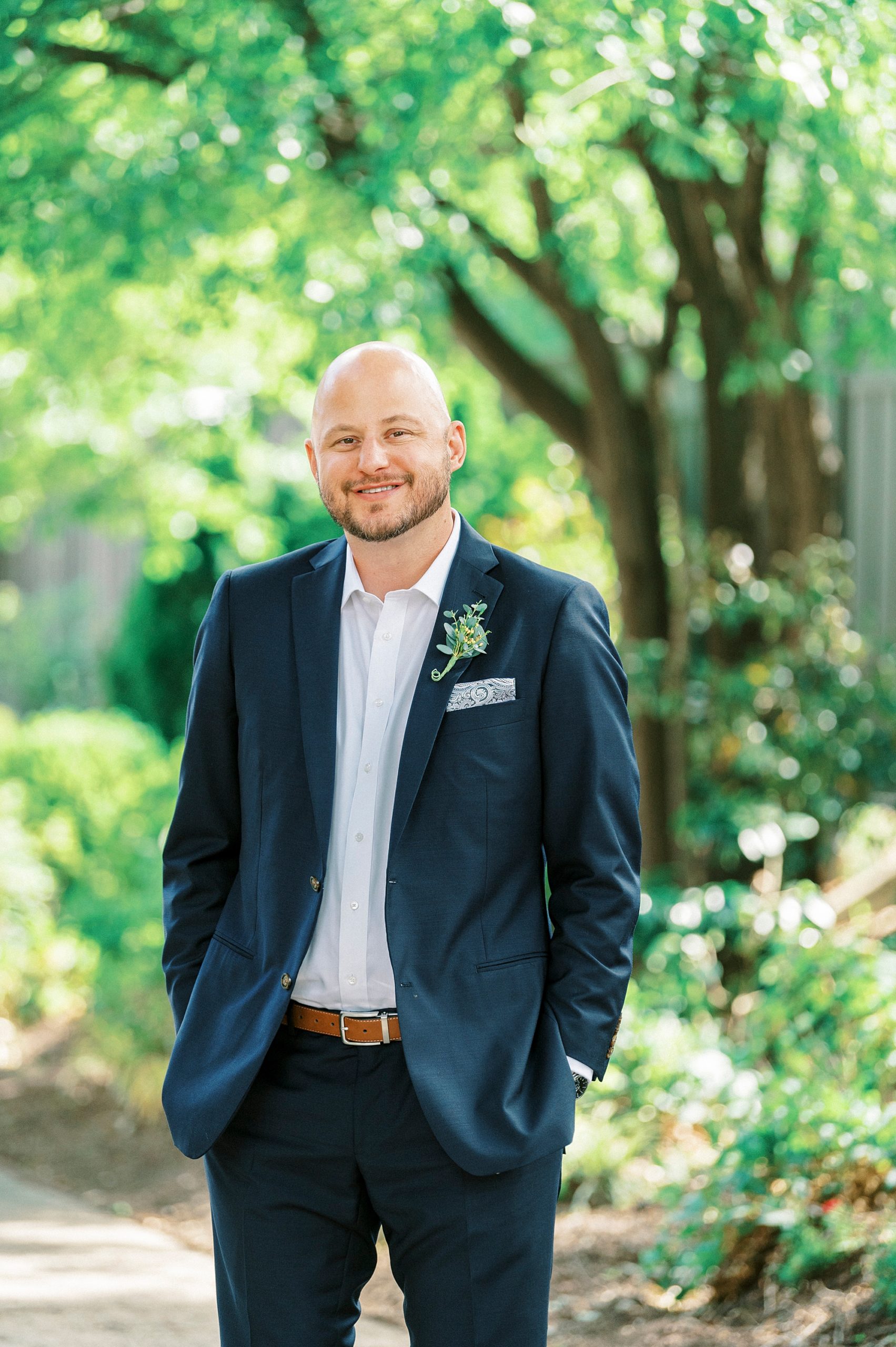 groom in navy jacket stands with hands in his pocket