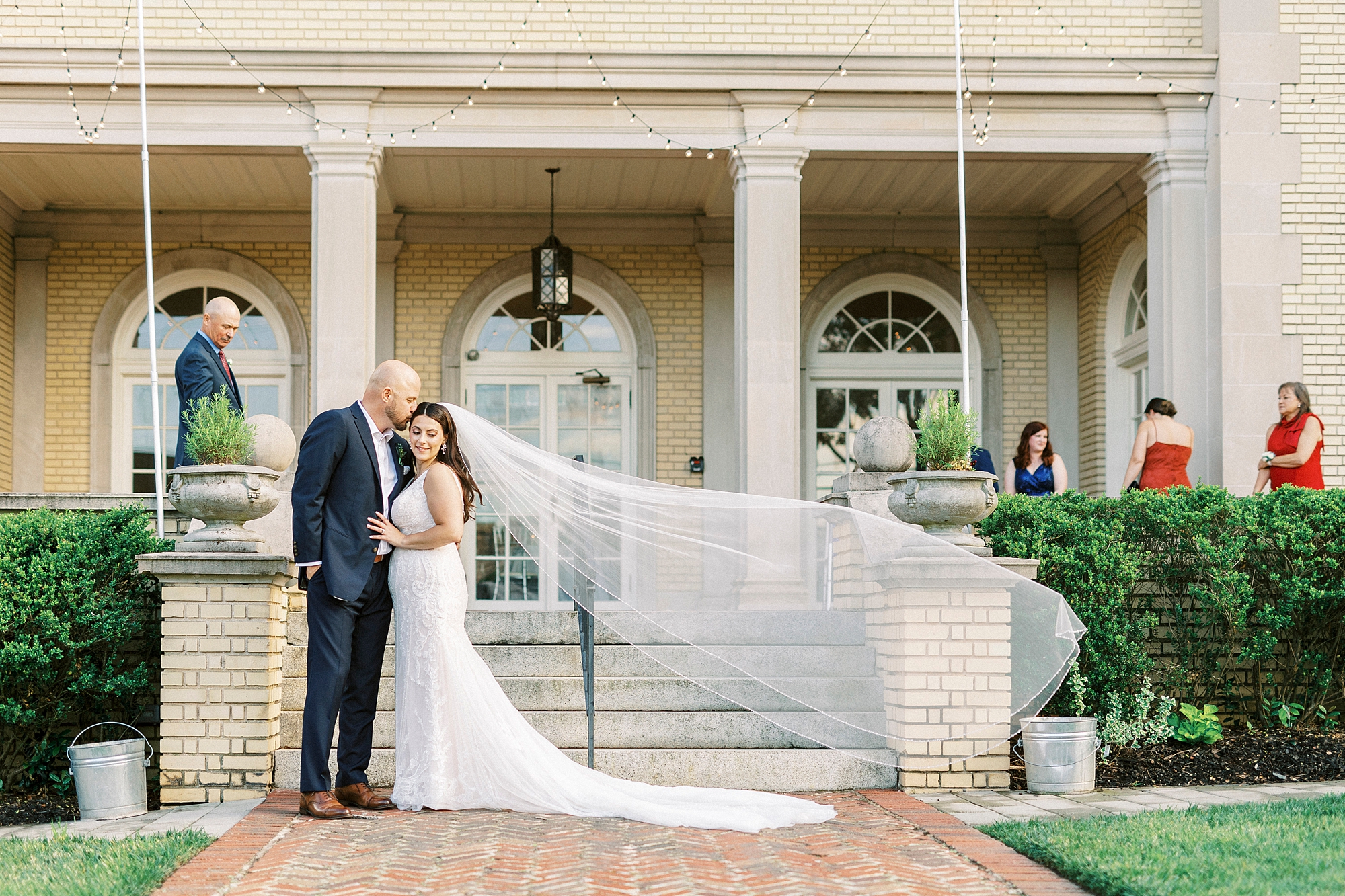 newlyweds hug outside Separk Mansion with bride's veil floating behind them