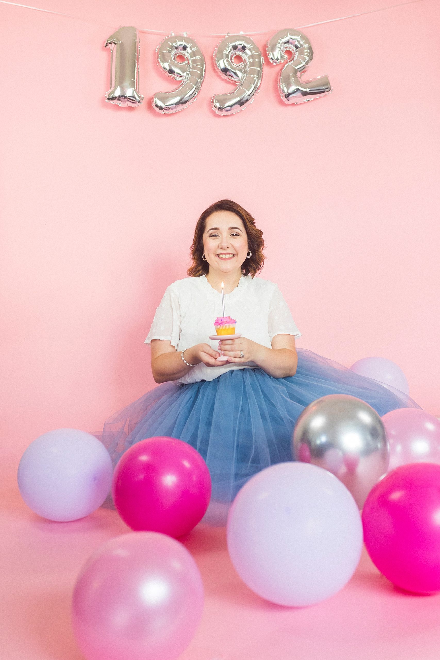 woman sits on pink backdrop during 30th birthday portraits 