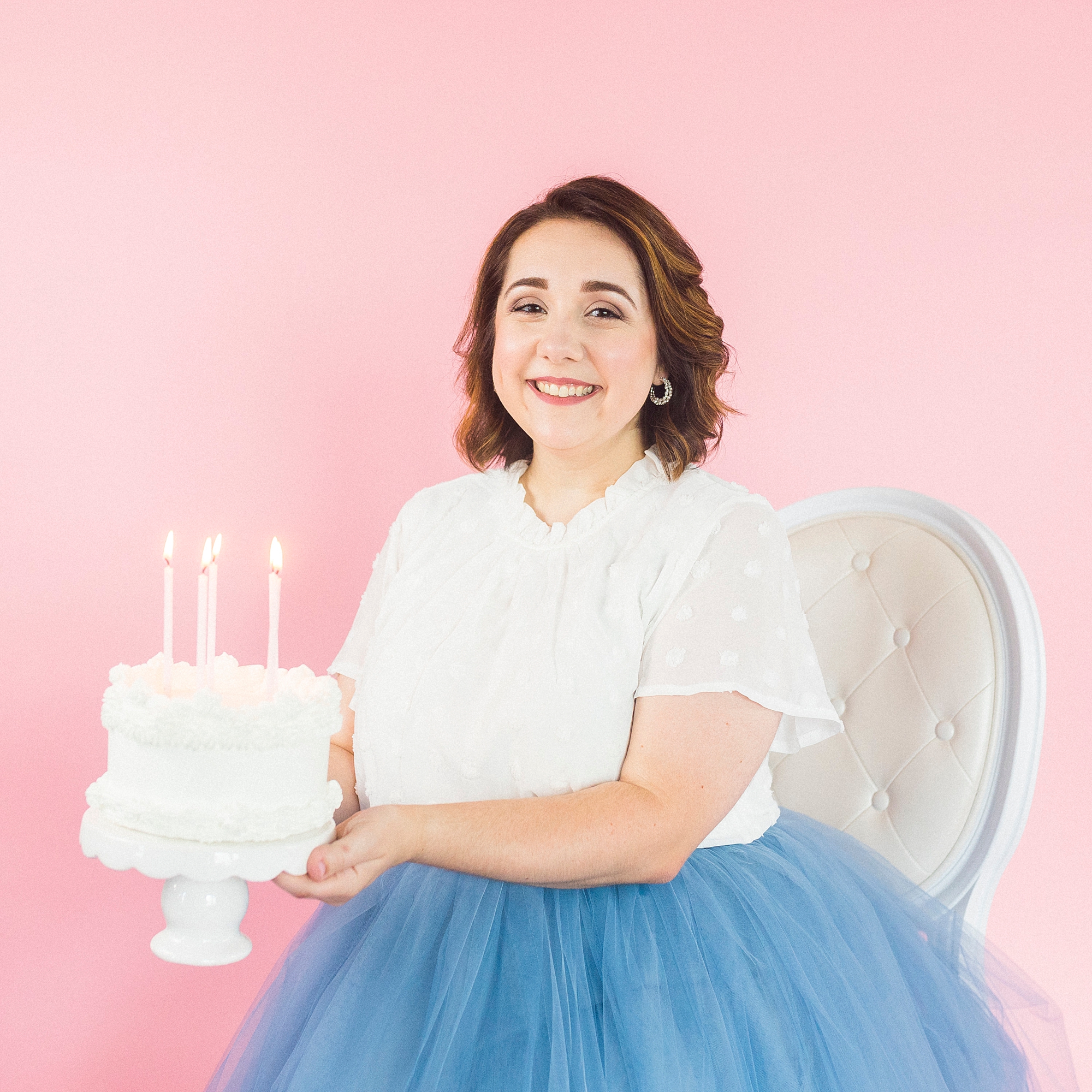 woman holds white cake with candles on pink backdrop during portraits in Charlotte NC