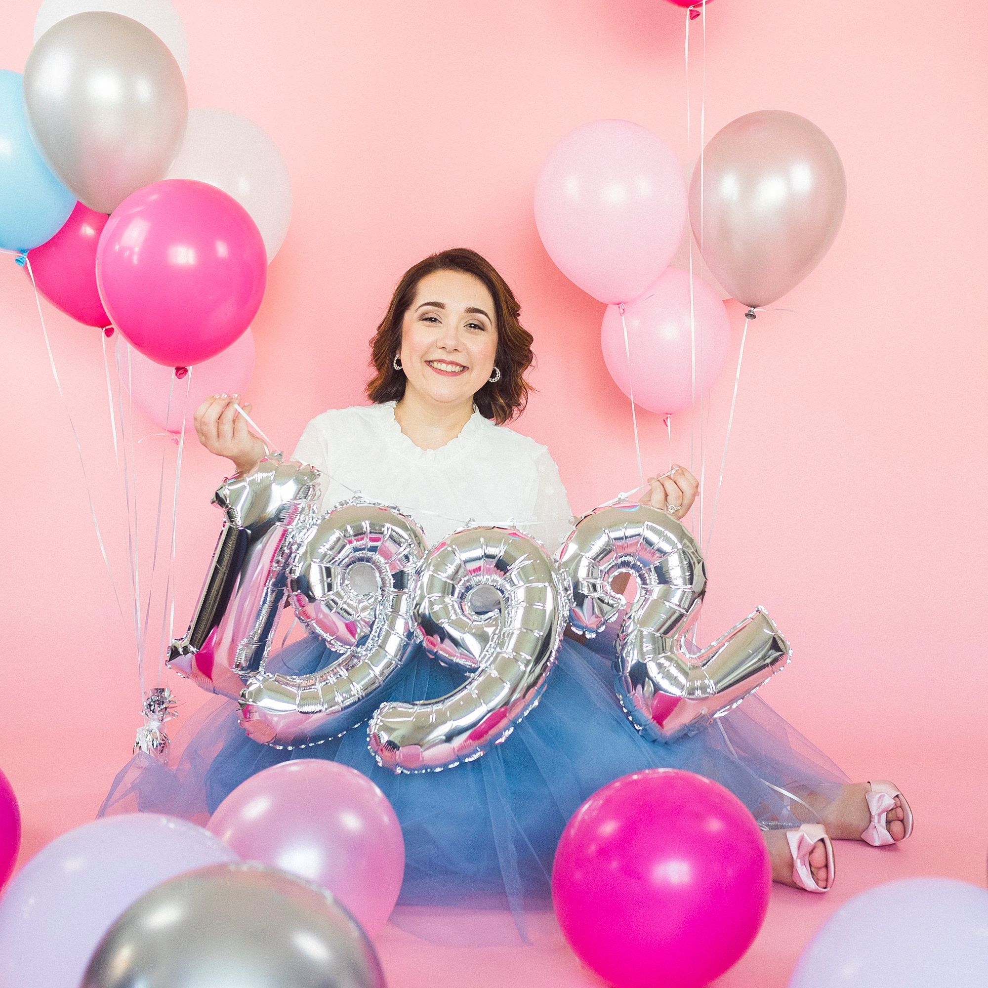 woman sits holding 1992 balloons
