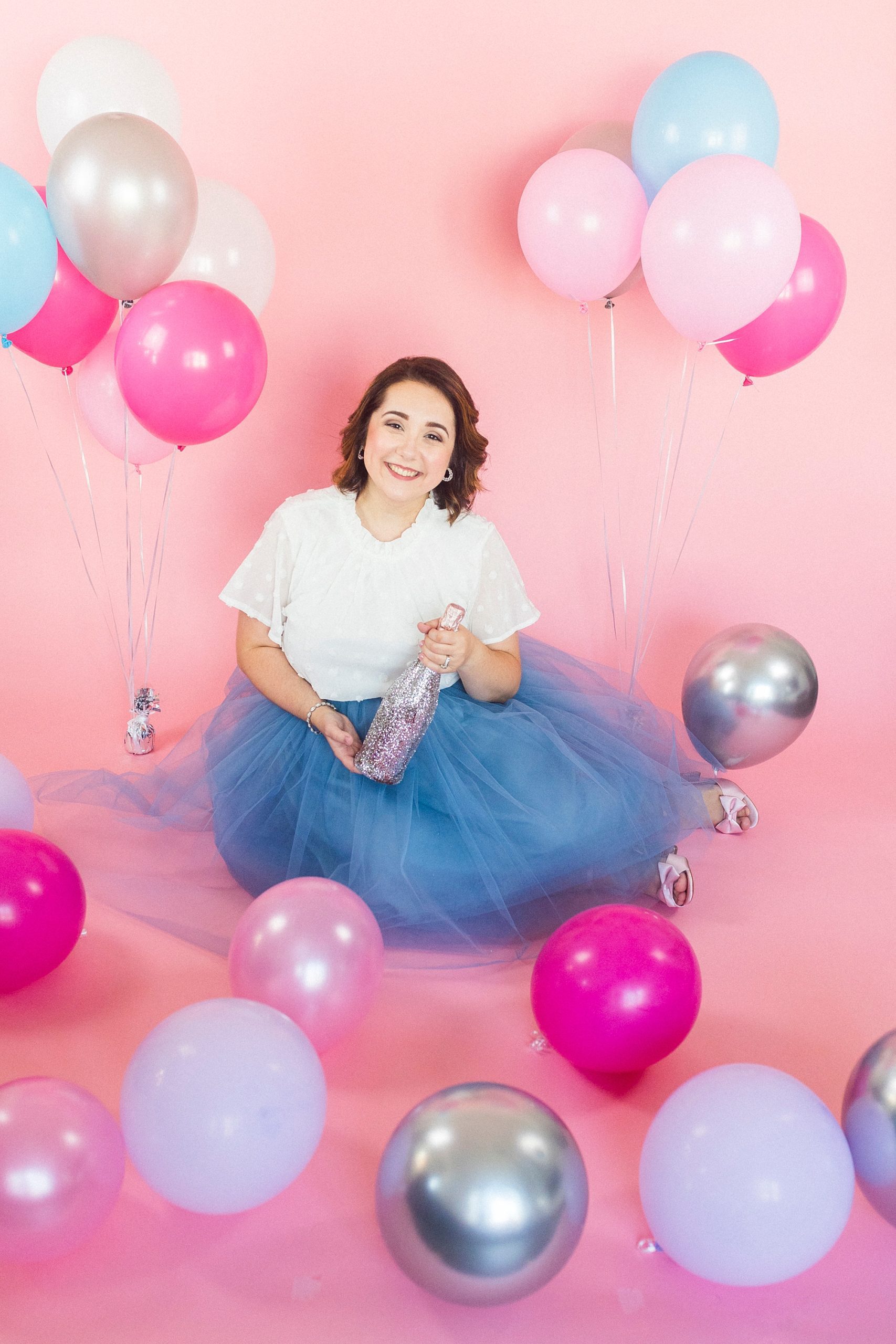 birthday girl sits on pink backdrop with balloons