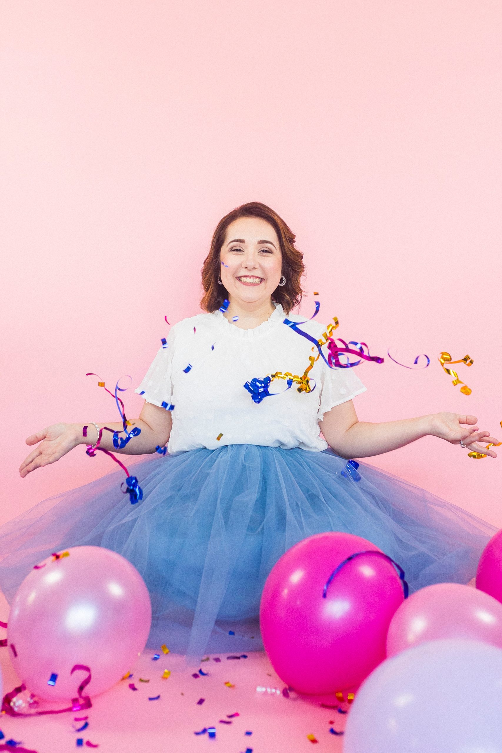 woman tosses confetti during 30th birthday portraits on pink backdrop