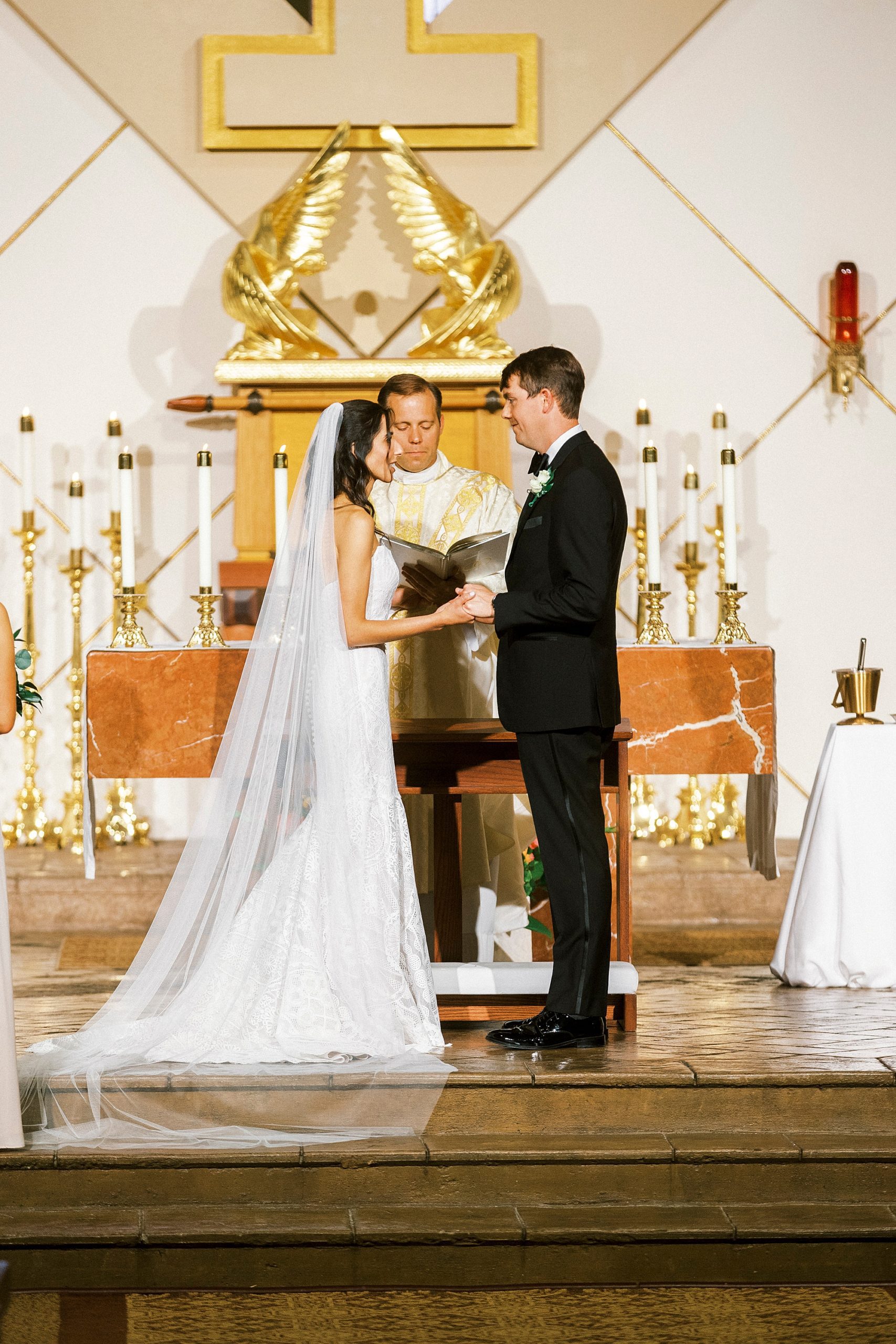 couple holds hands during vows at traditional church wedding at St. Gabriel Catholic Church