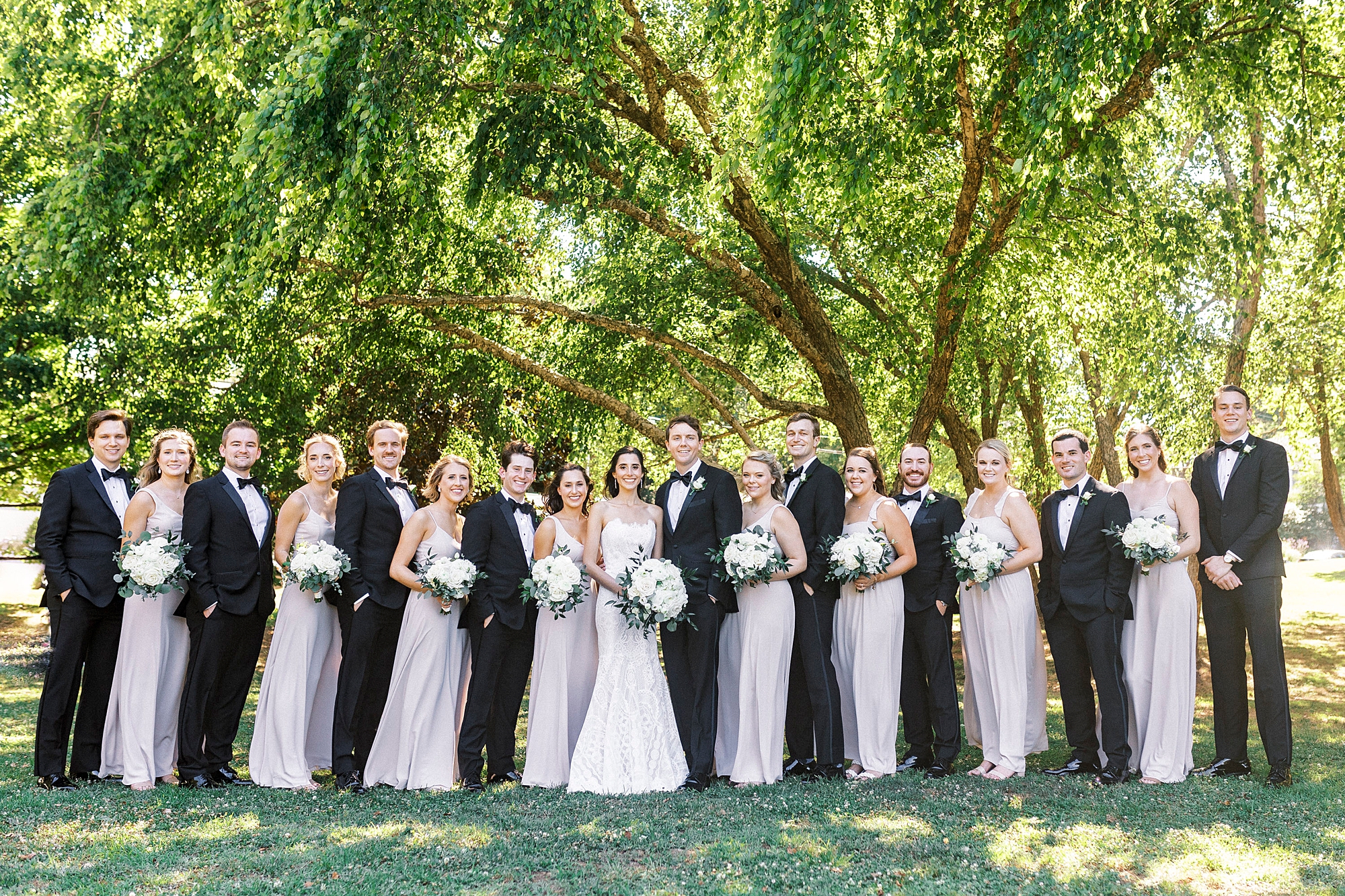 newlyweds stand with wedding party in classic tuxes and pink gowns