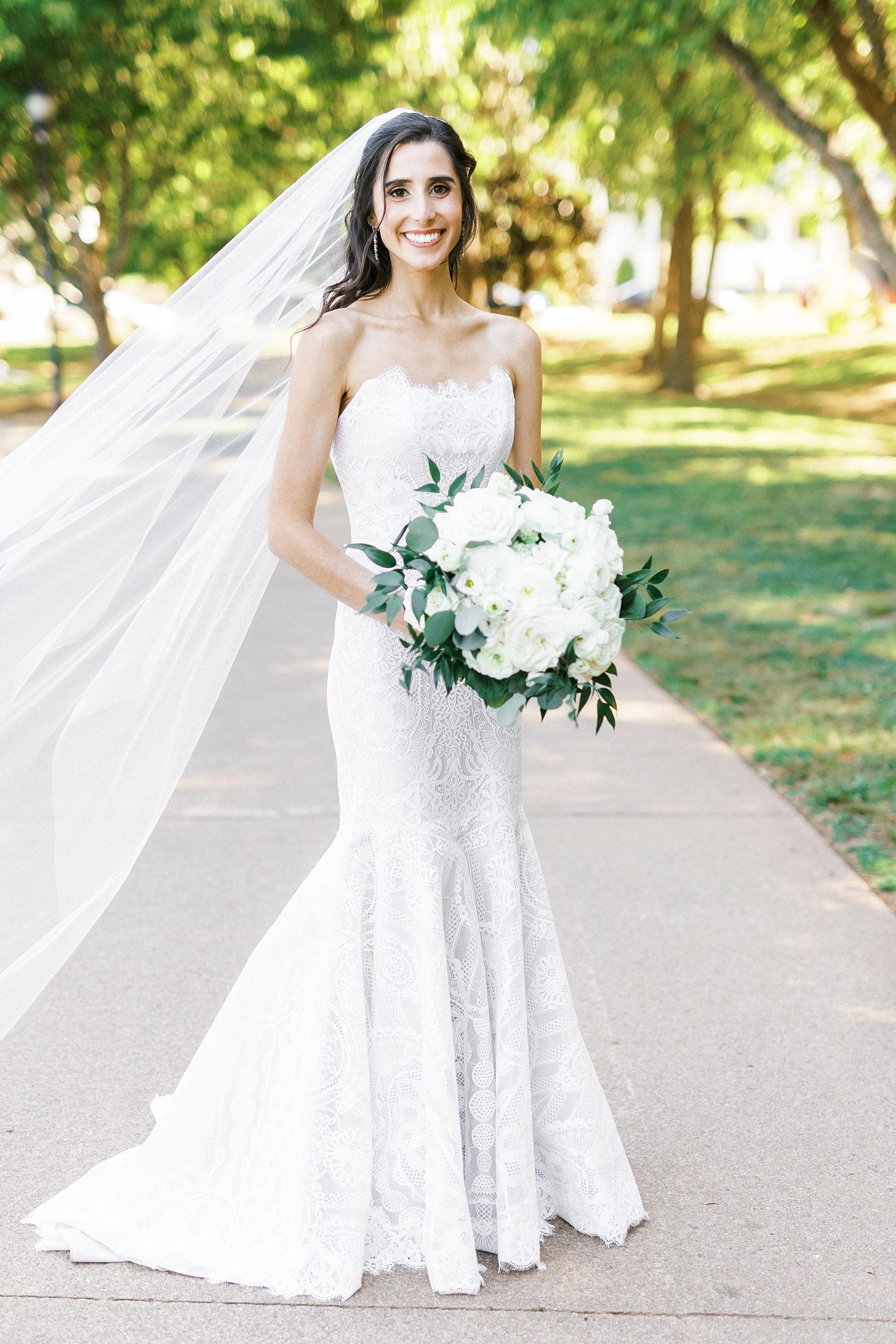 bride poses on sidewalk in wedding gown with veil draped behind her at Freedom Park