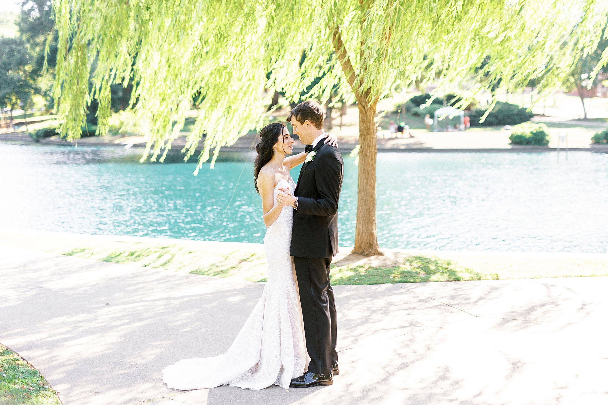 bride and groom stand on sidewalk by pond in Freedom Park