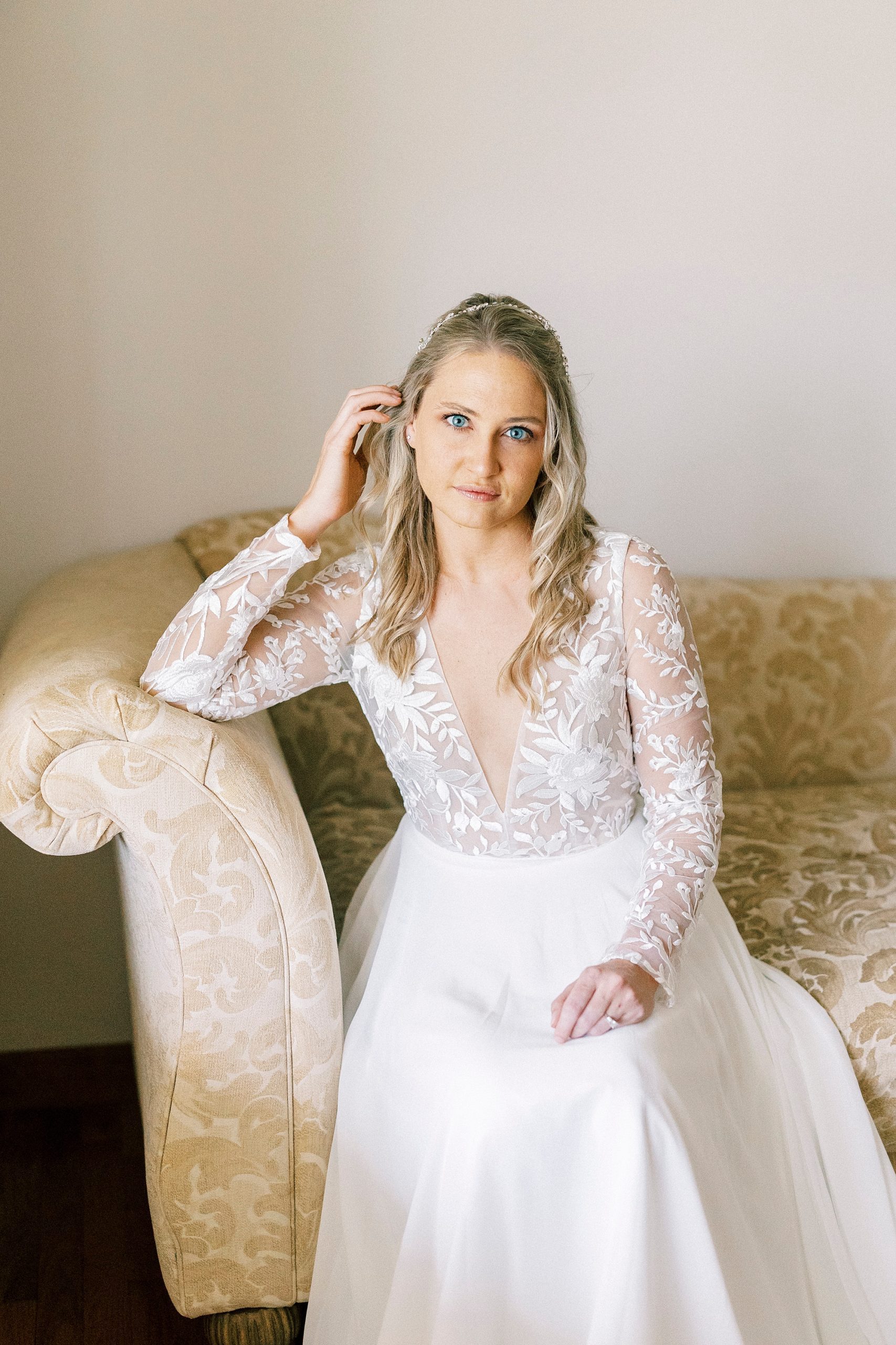 bride sits on gold and white couch during elegant bridal portraits