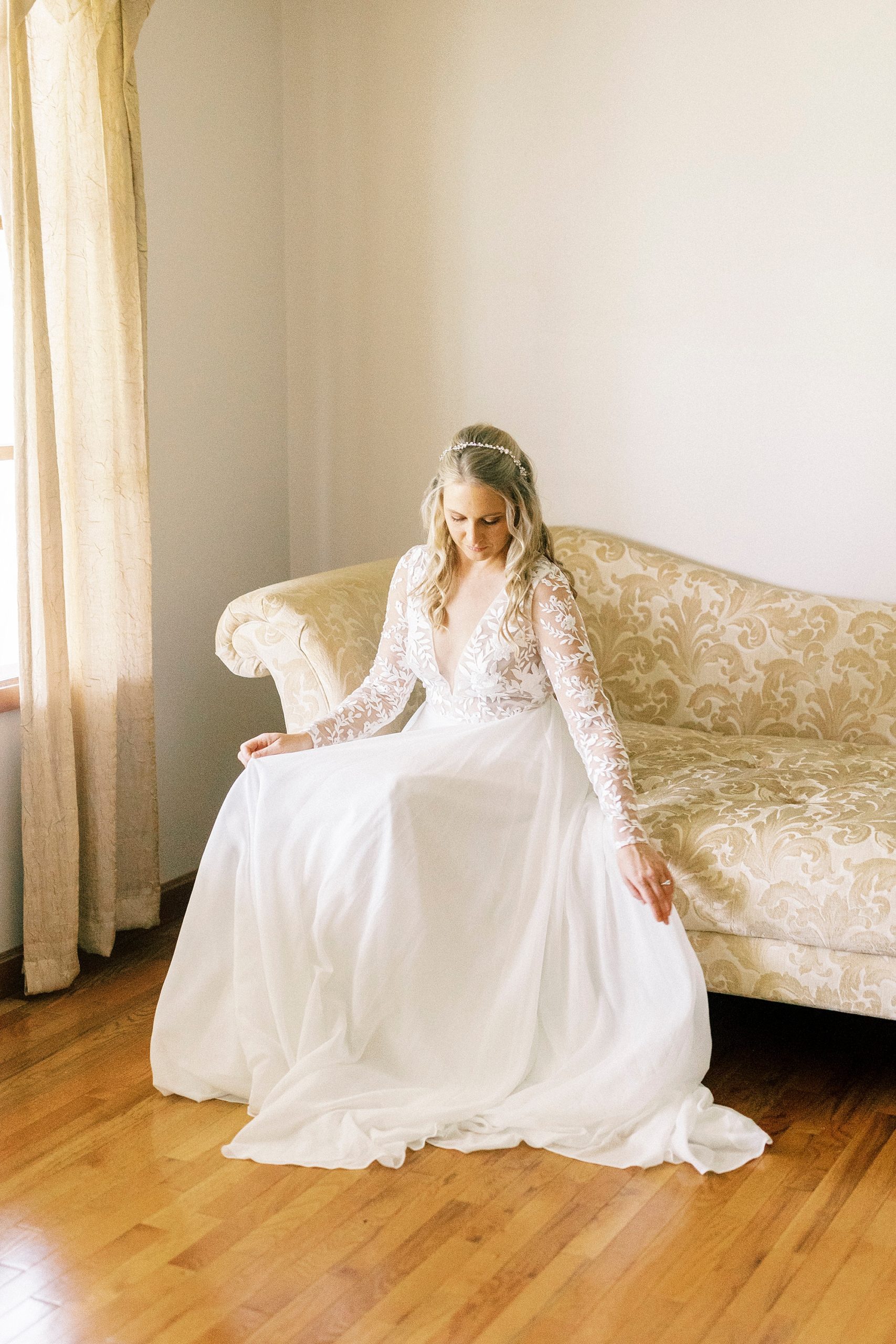 bride looks down at skirt during bridal portraits on couch in Lenoir home