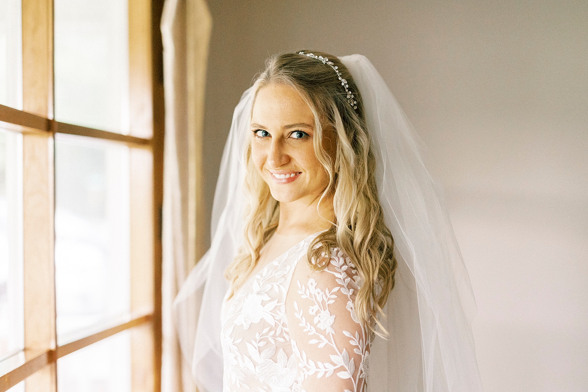 bride smiles by window at home during bridal portraits