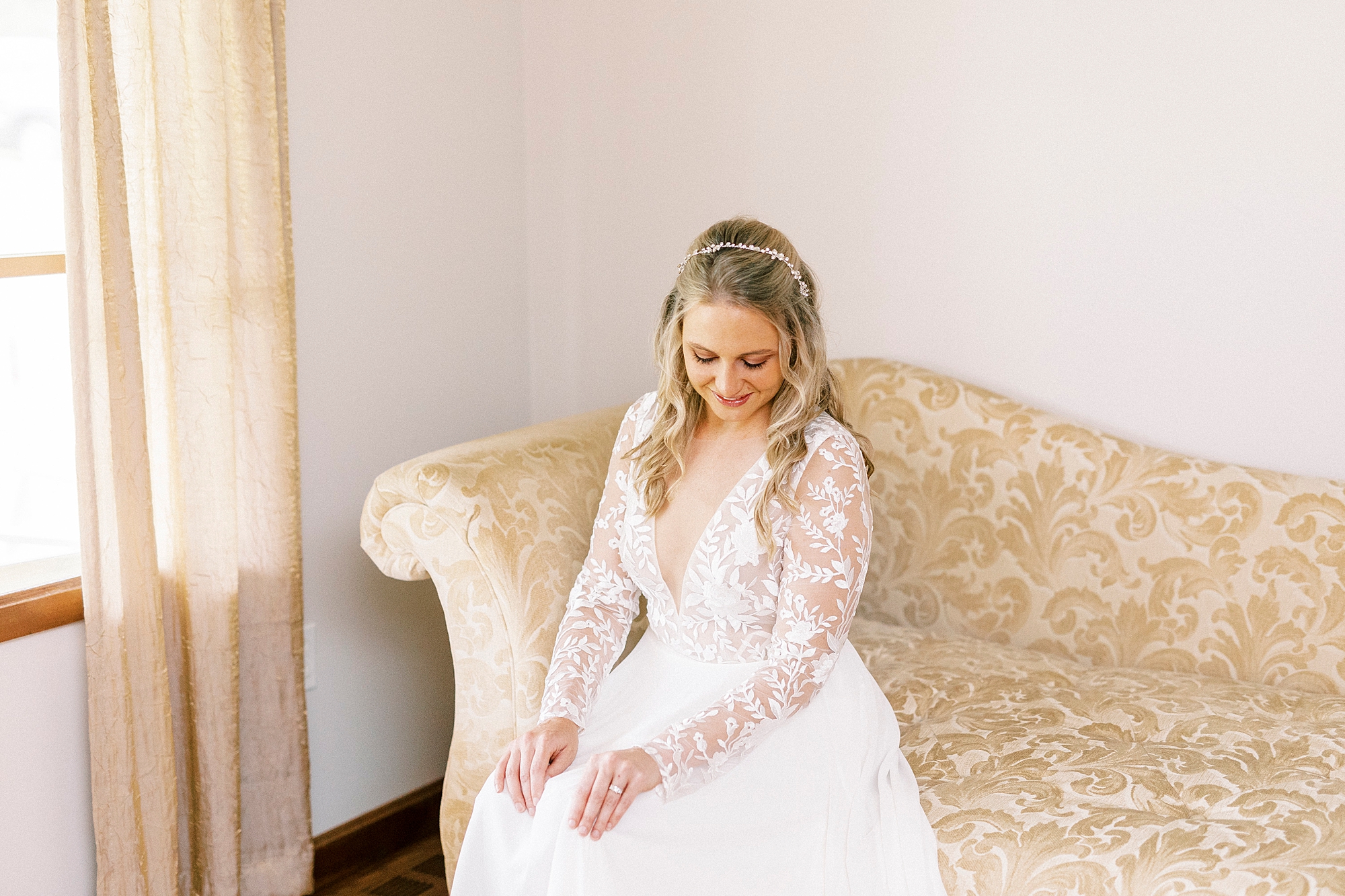 bride looks down at lap in wedding gown sitting on couch
