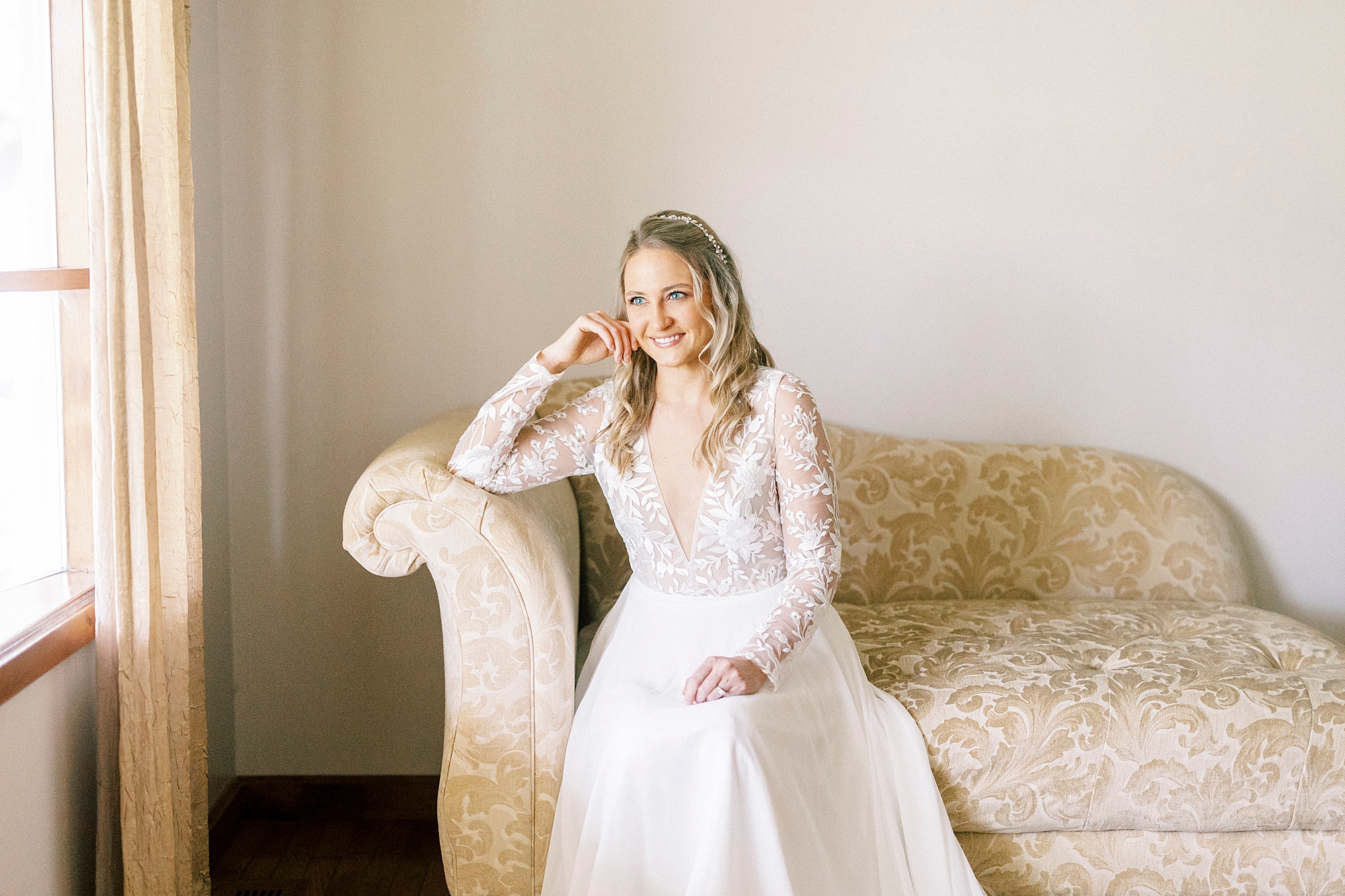 bride laughs sitting on couch during elegant bridal portraits at home