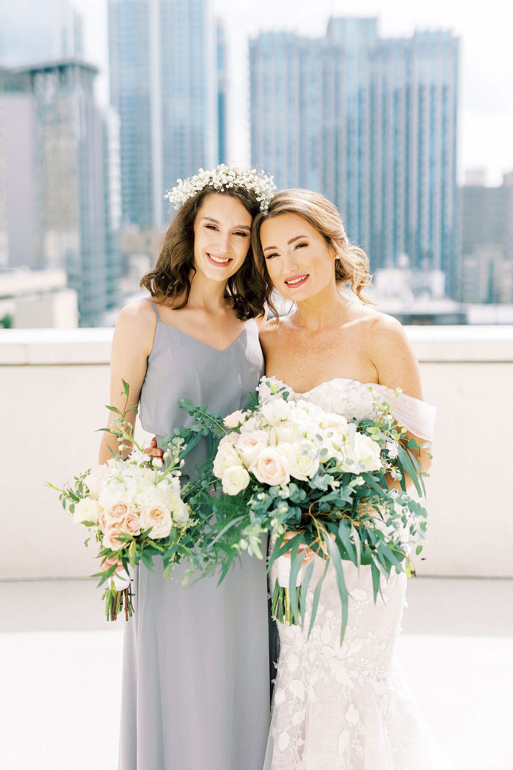 bride poses with sister with Charlotte skyline behind them