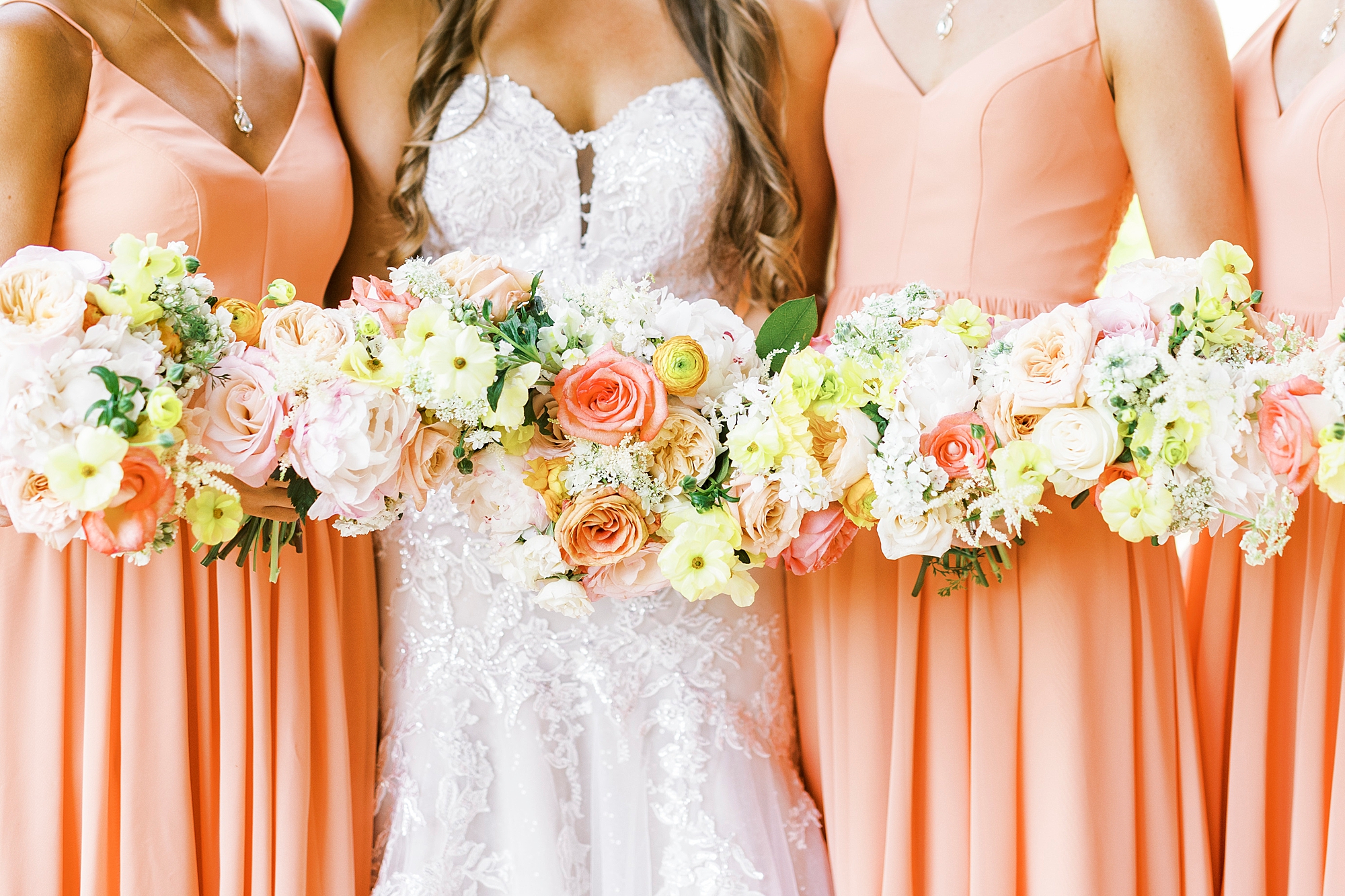 bride and bridesmaids hold yellow and pink bouquets 