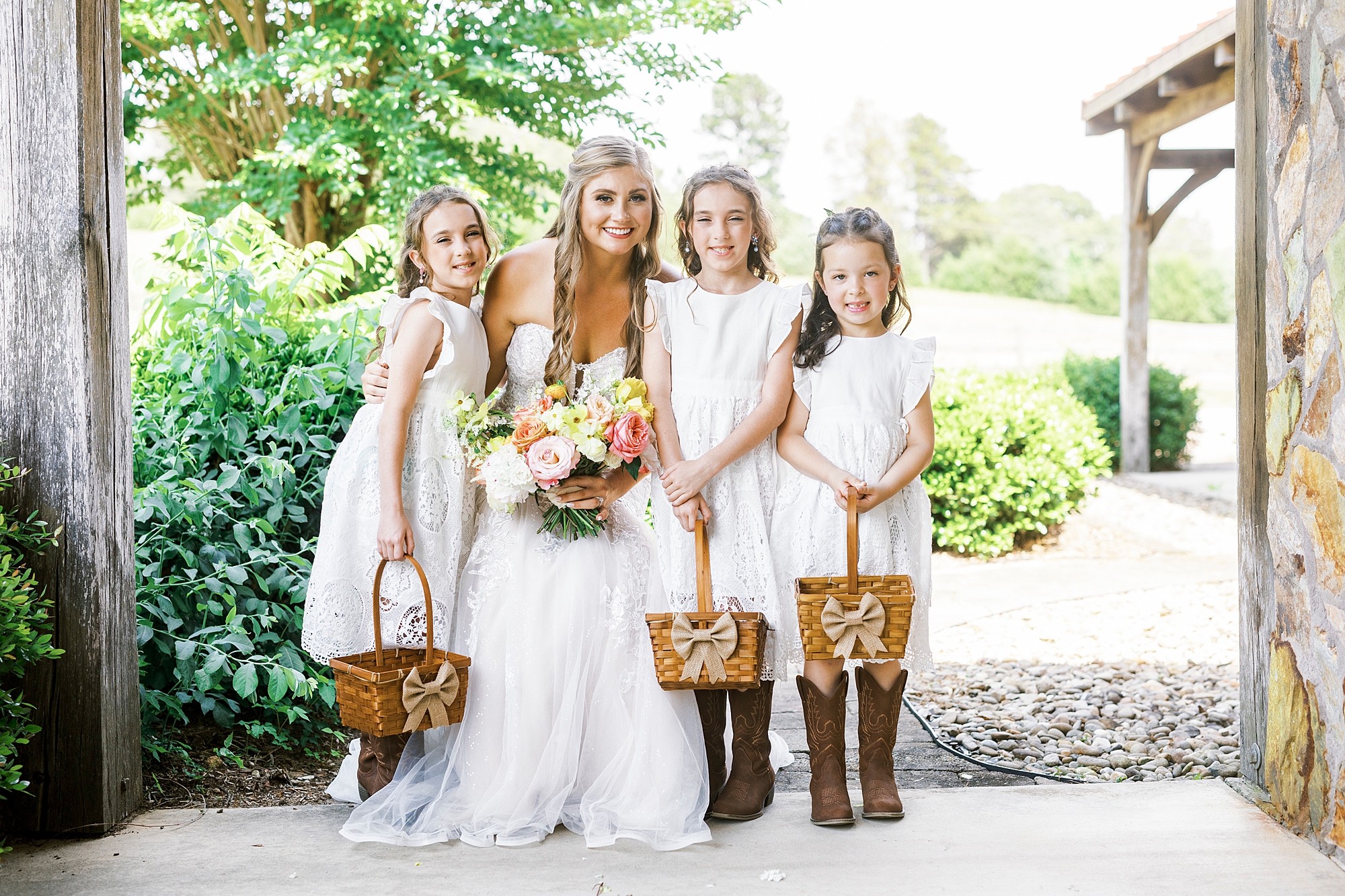 bride poses with flower girls in white dresses with cowboy boots