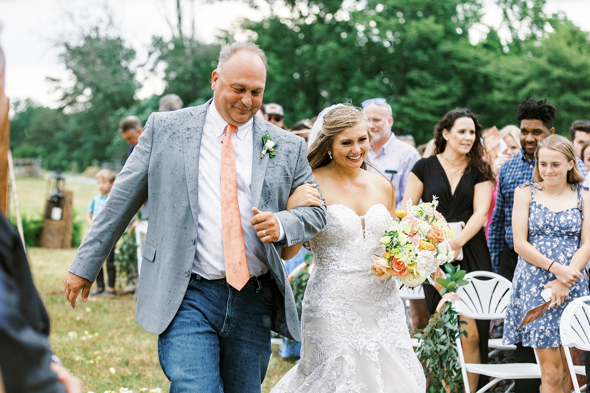 bride and dad laugh walking down aisle during rainy wedding ceremony at The Stable at Riverview