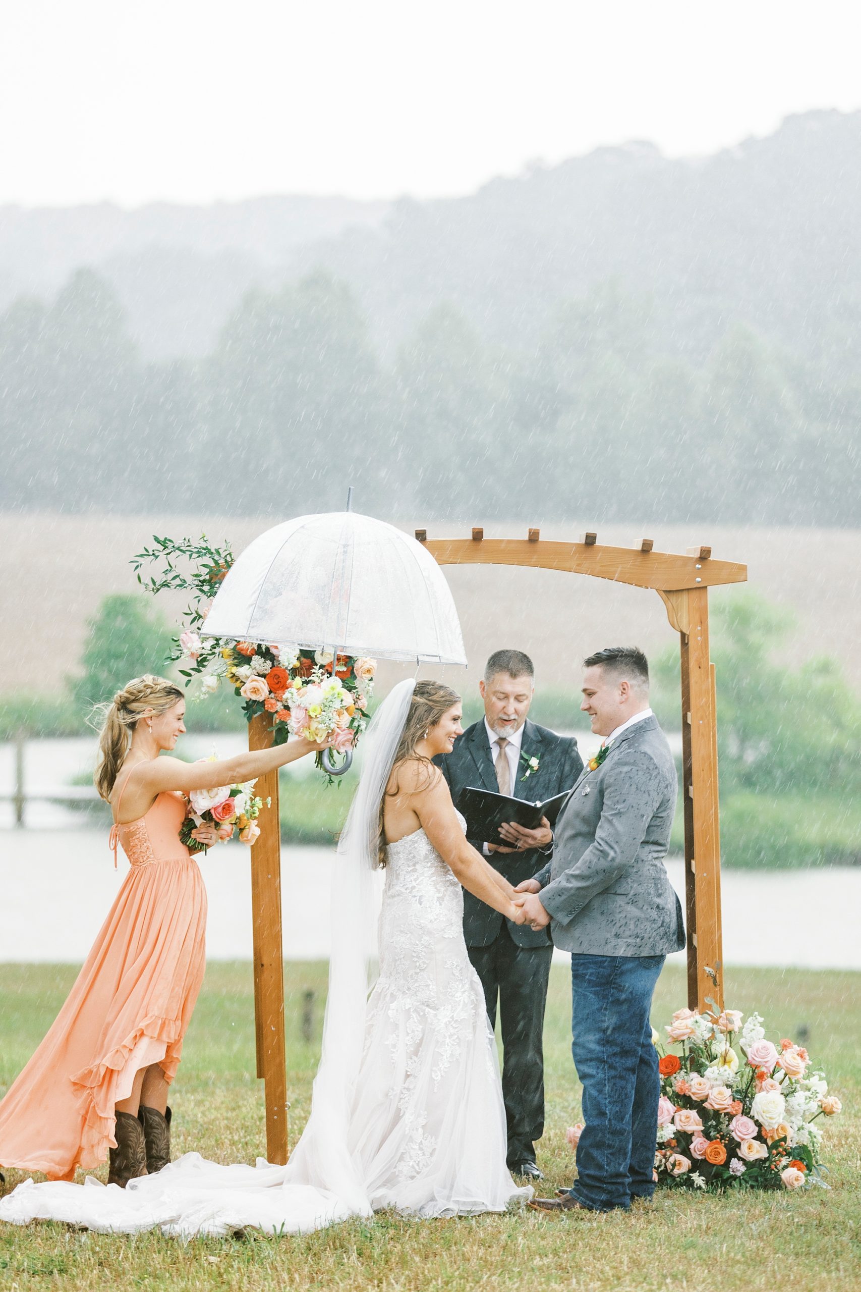 bridesmaid holds umbrella over bride during rainy wedding ceremony at The Stable at Riverview
