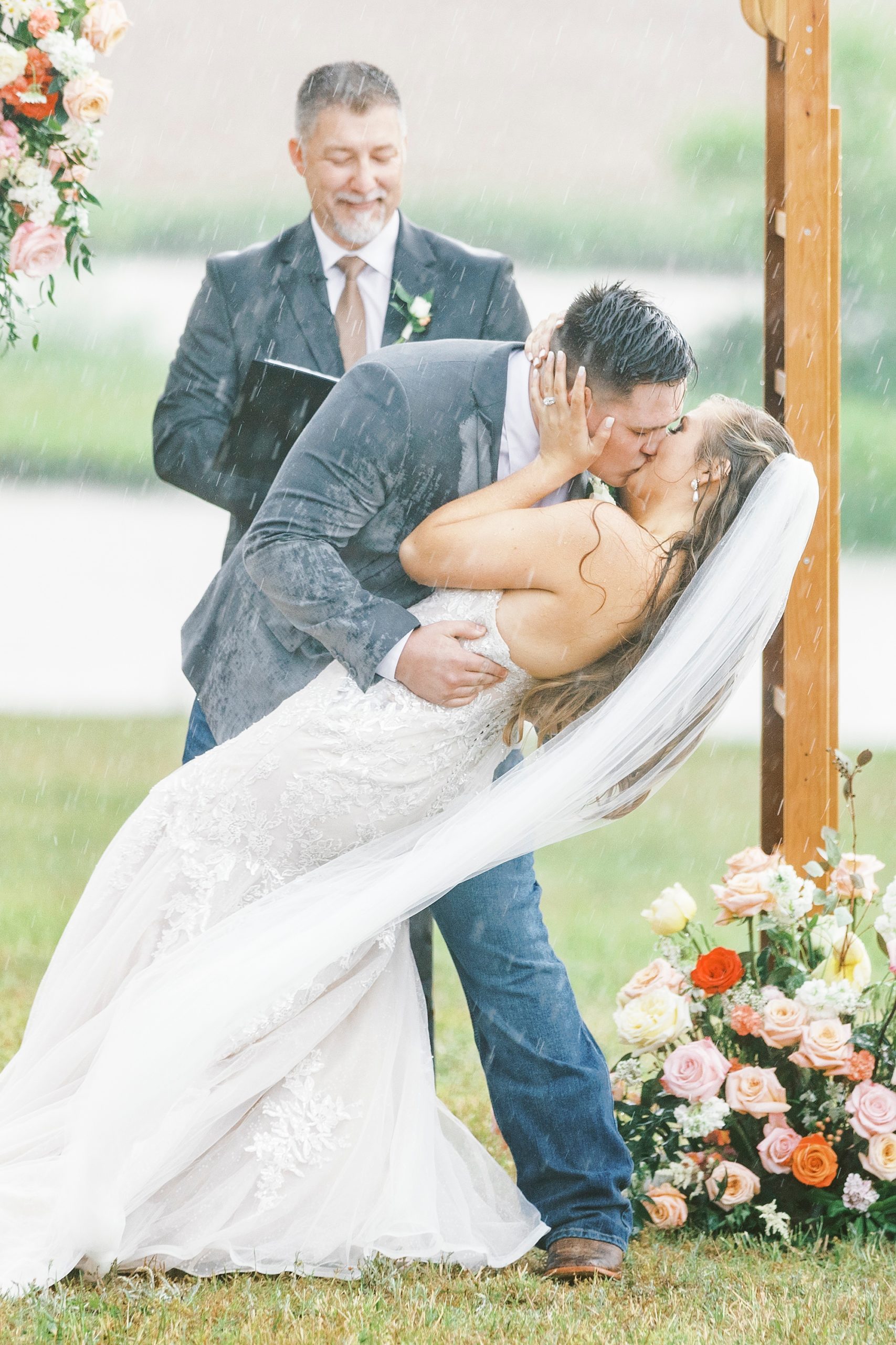 bride and groom kiss dipping backwards during rainy wedding ceremony at The Stable at Riverview