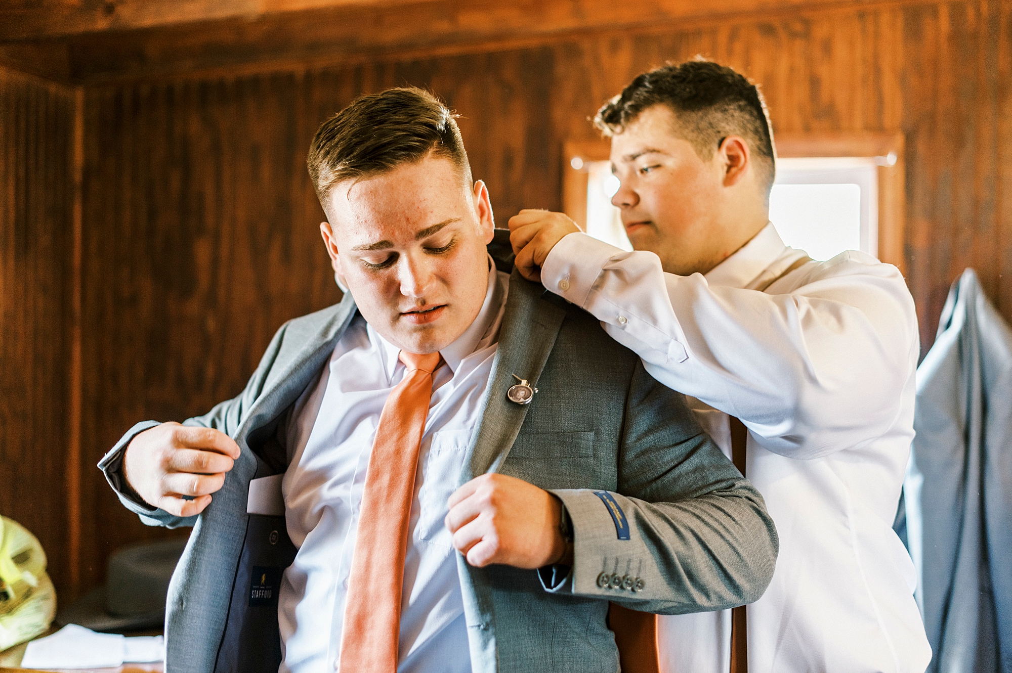 groomsman helps groom with suit and tie