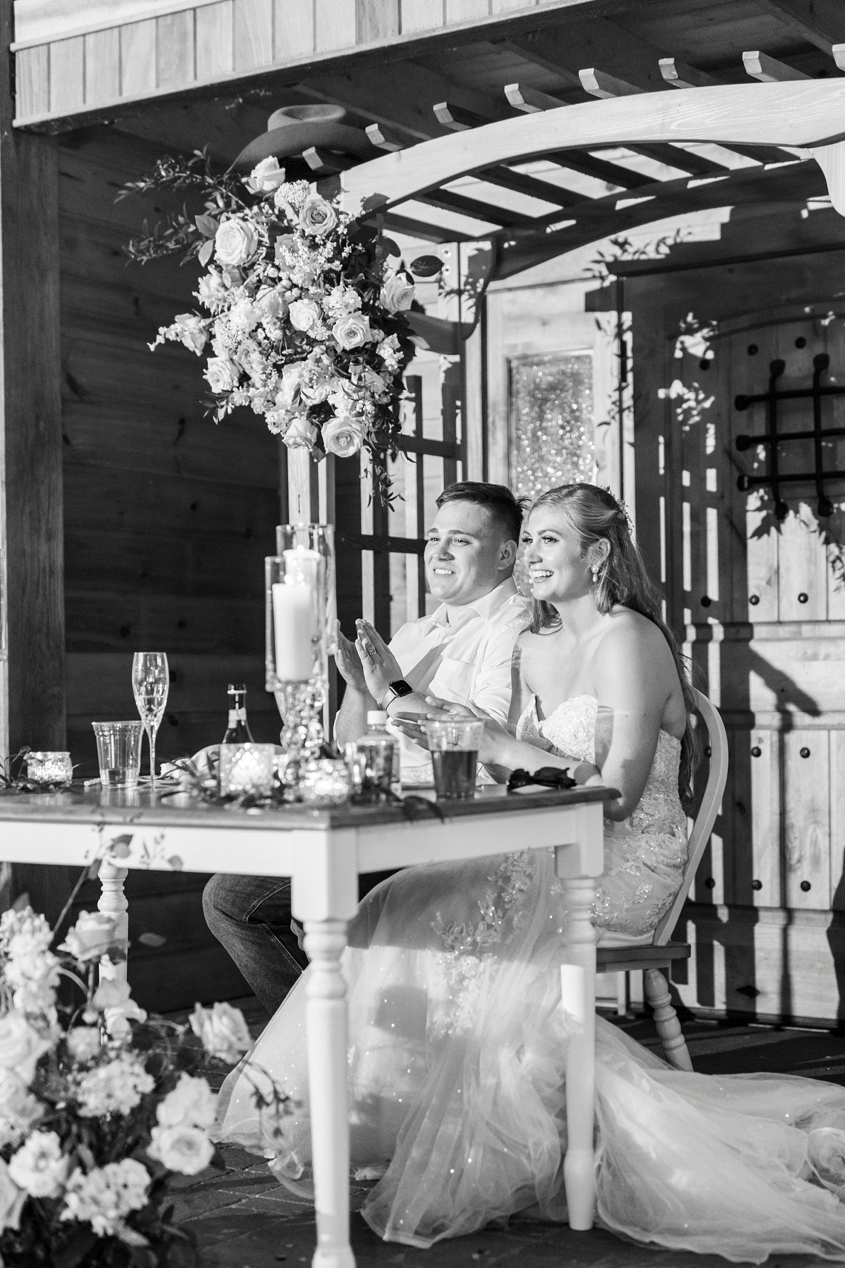 newlyweds sit at sweetheart table during reception at The Stable at Riverview