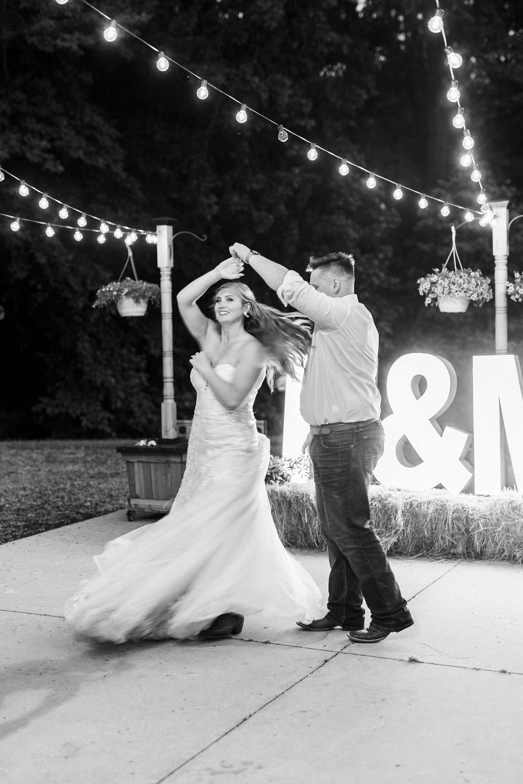 groom twirls bride dancing by marquee lights