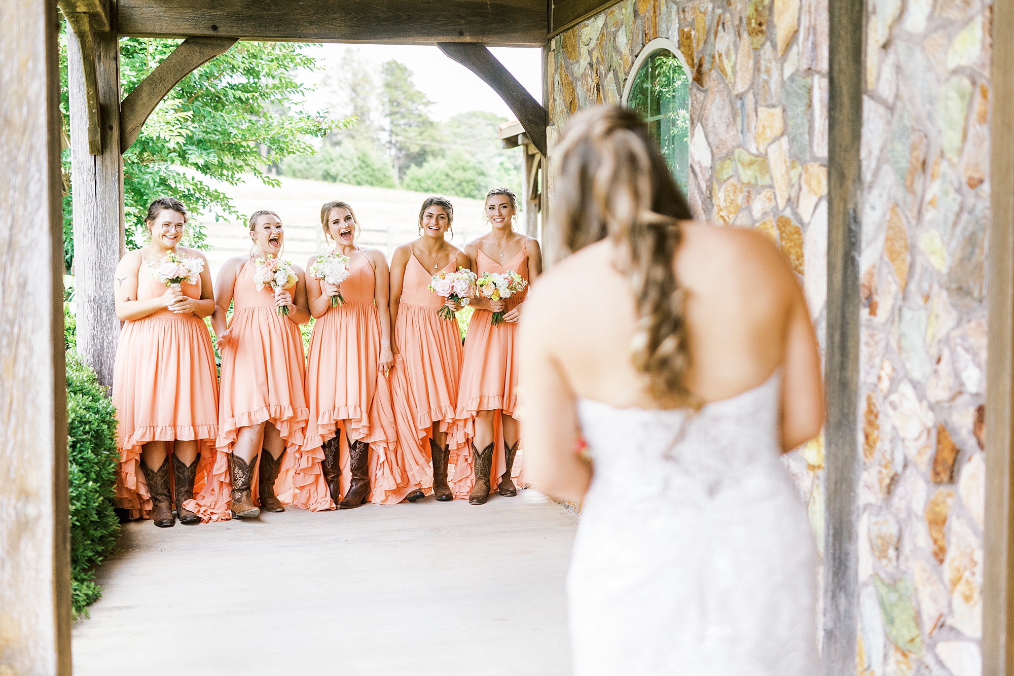 bride has first look with bridesmaids in coral gowns outside The Stable at Riverview