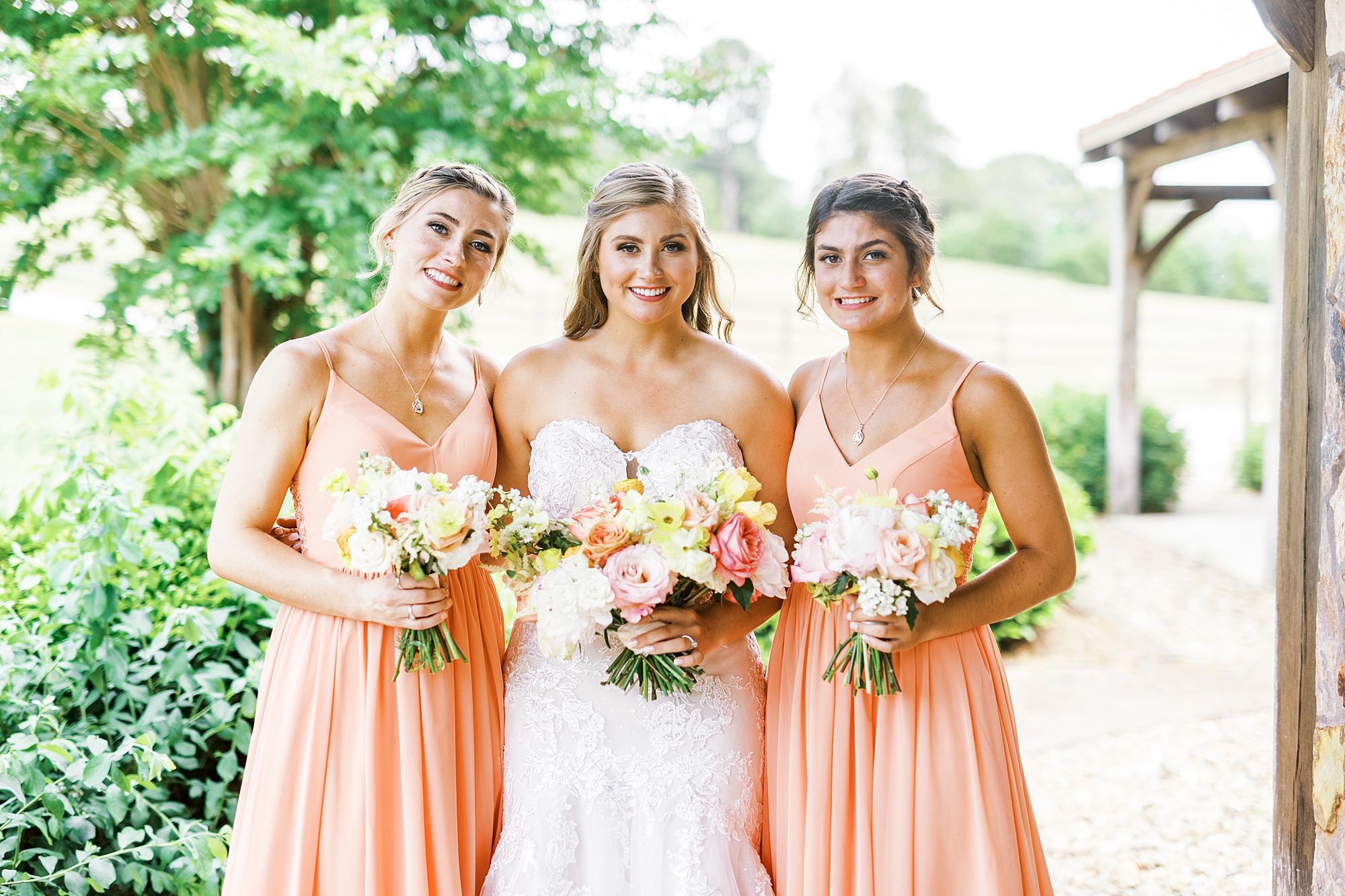 bride stands with bridesmaids in coral dresses