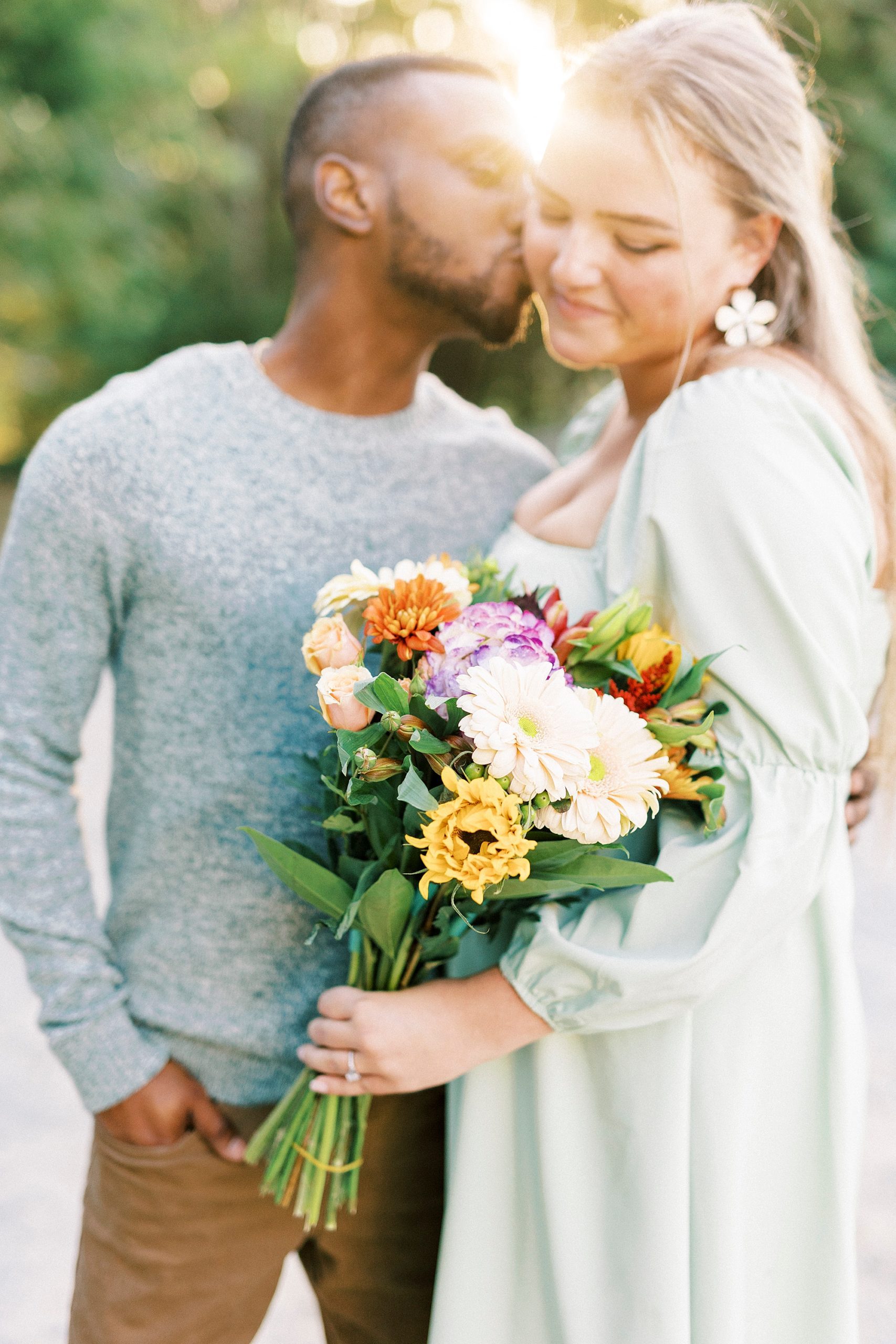 groom kisses fiancee while she holds bouquet of wild flowers