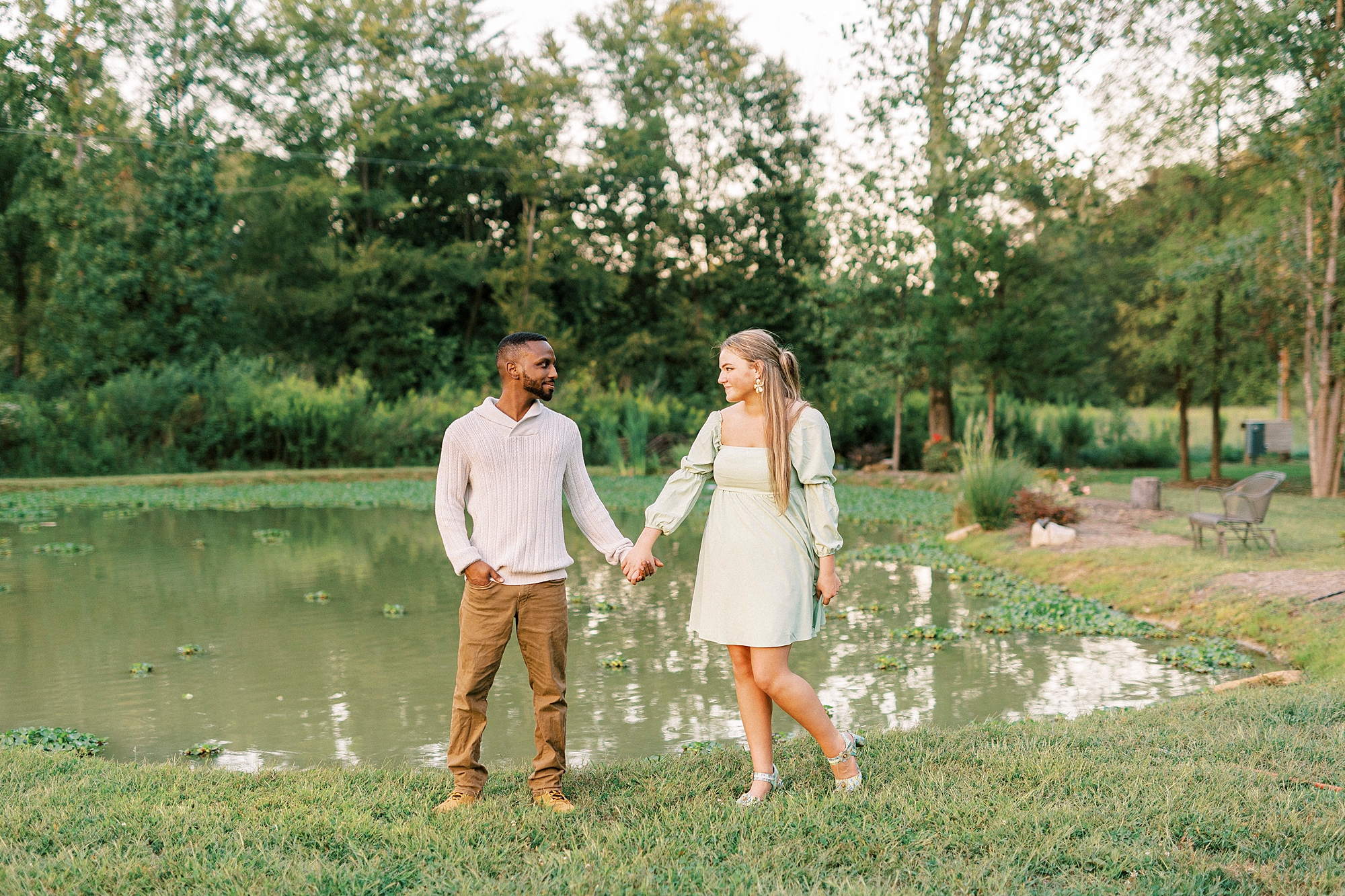 engaged couple holds hands at pond 