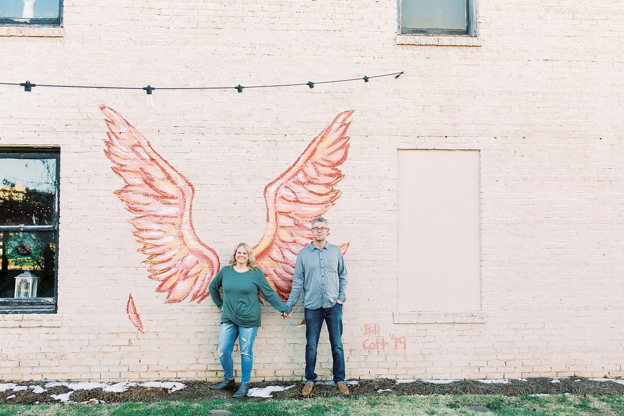 couple poses by angel wings on mural in Monroe NC