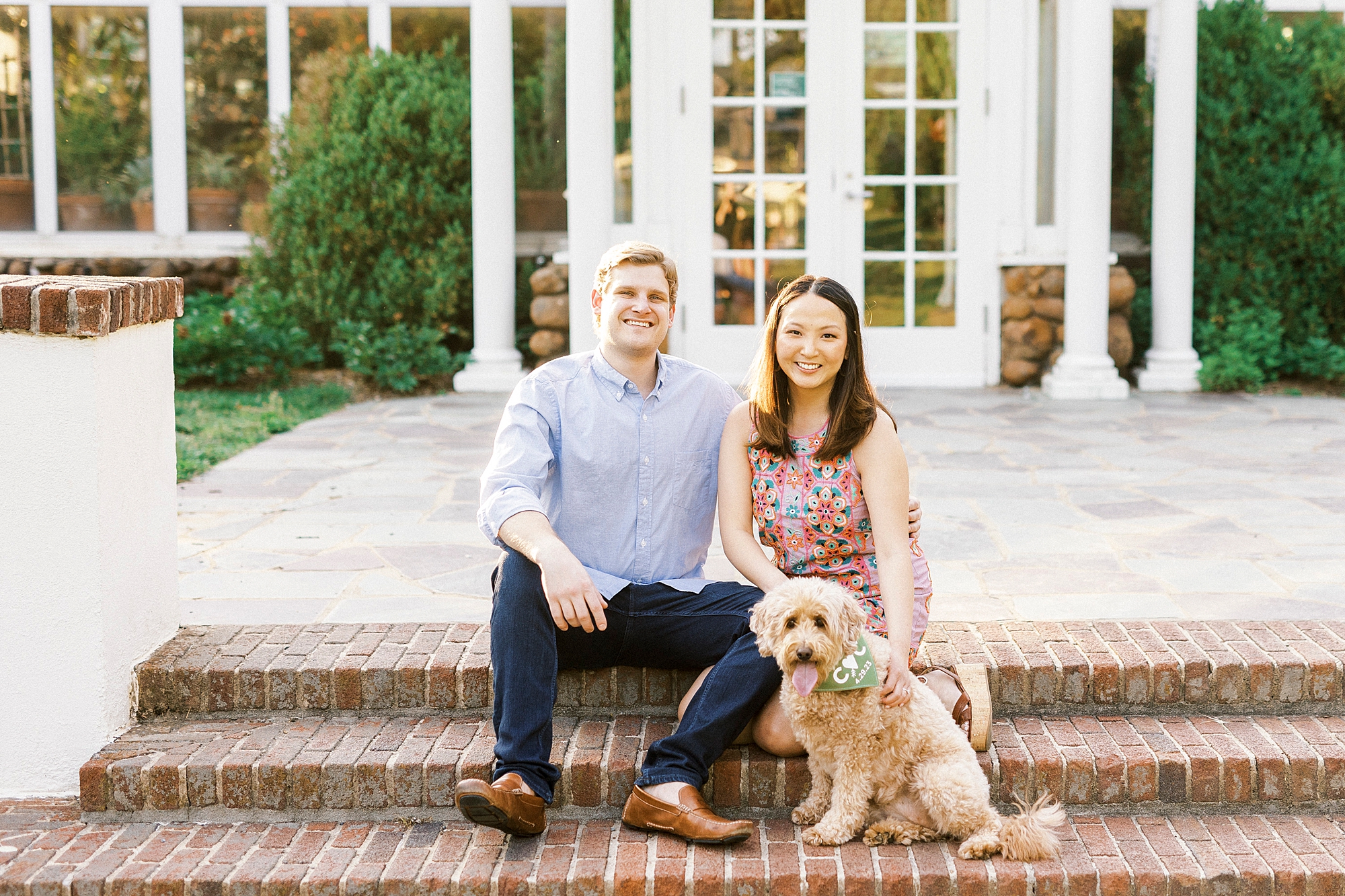 engaged couple sits together with dog on brick staircase at Reynolda Gardens