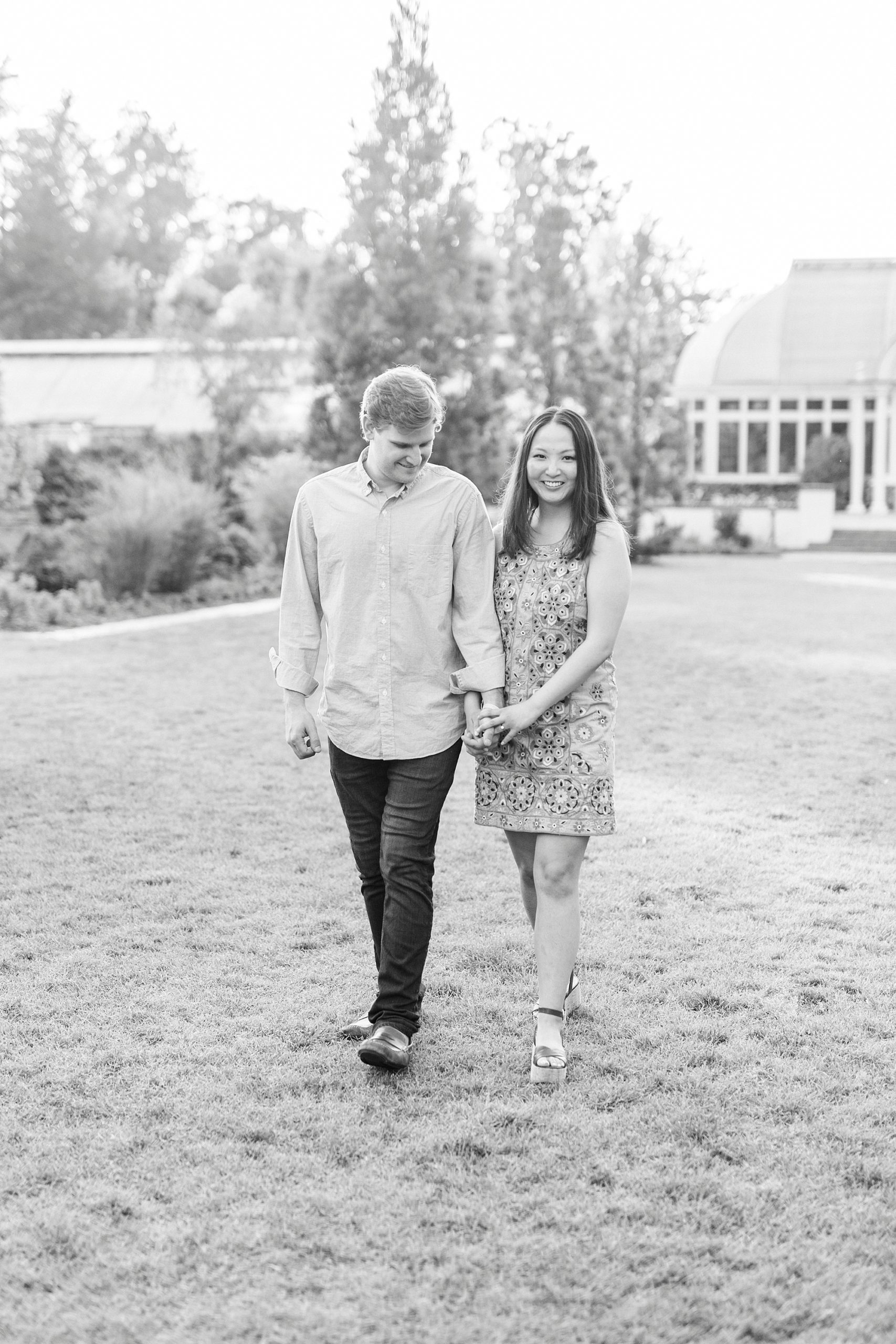 engaged couple holds hands walking across lawn at Reynolda Gardens