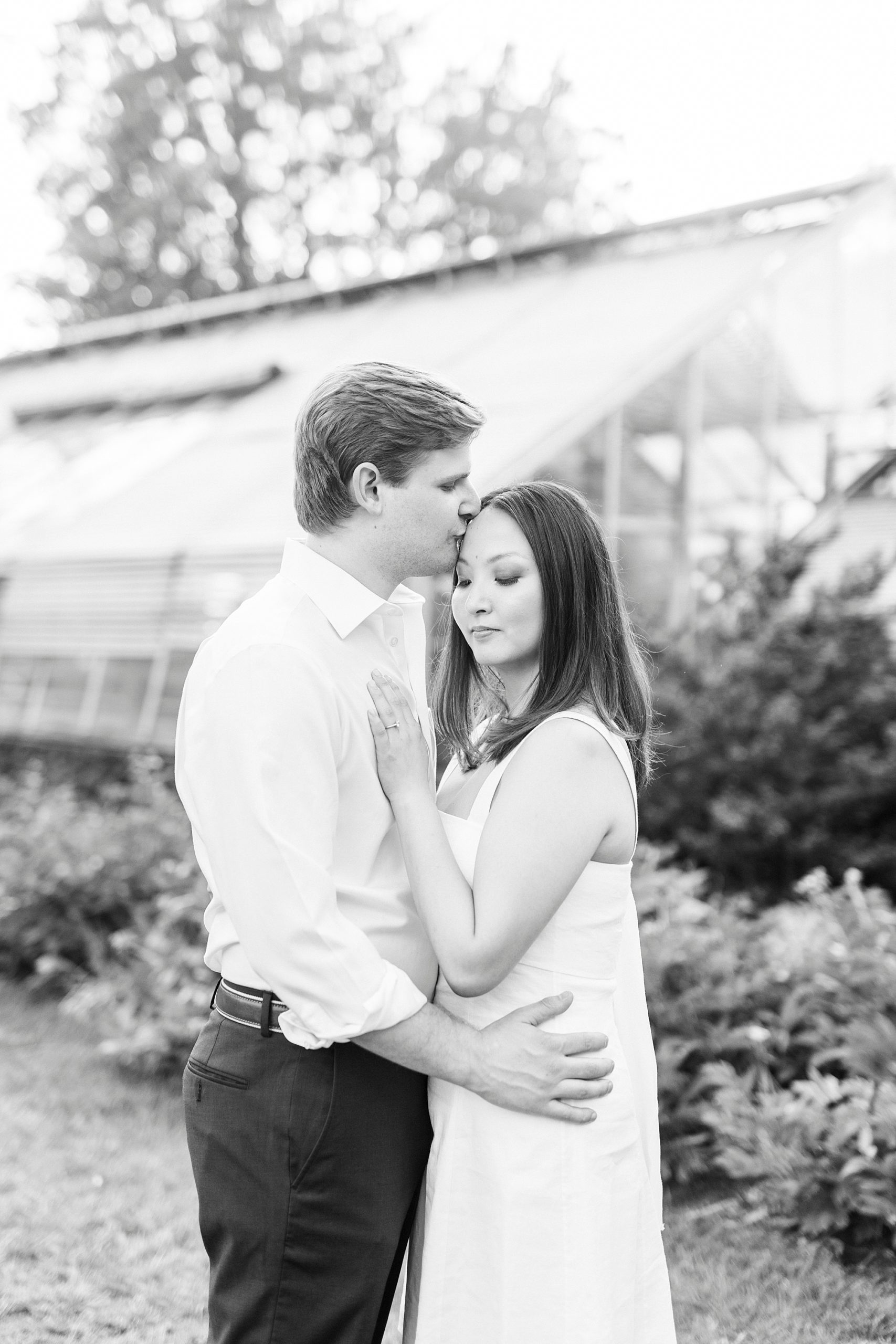 groom kisses fiancee on forehead in black and white portraits by greenhouse at Reynolda Gardens