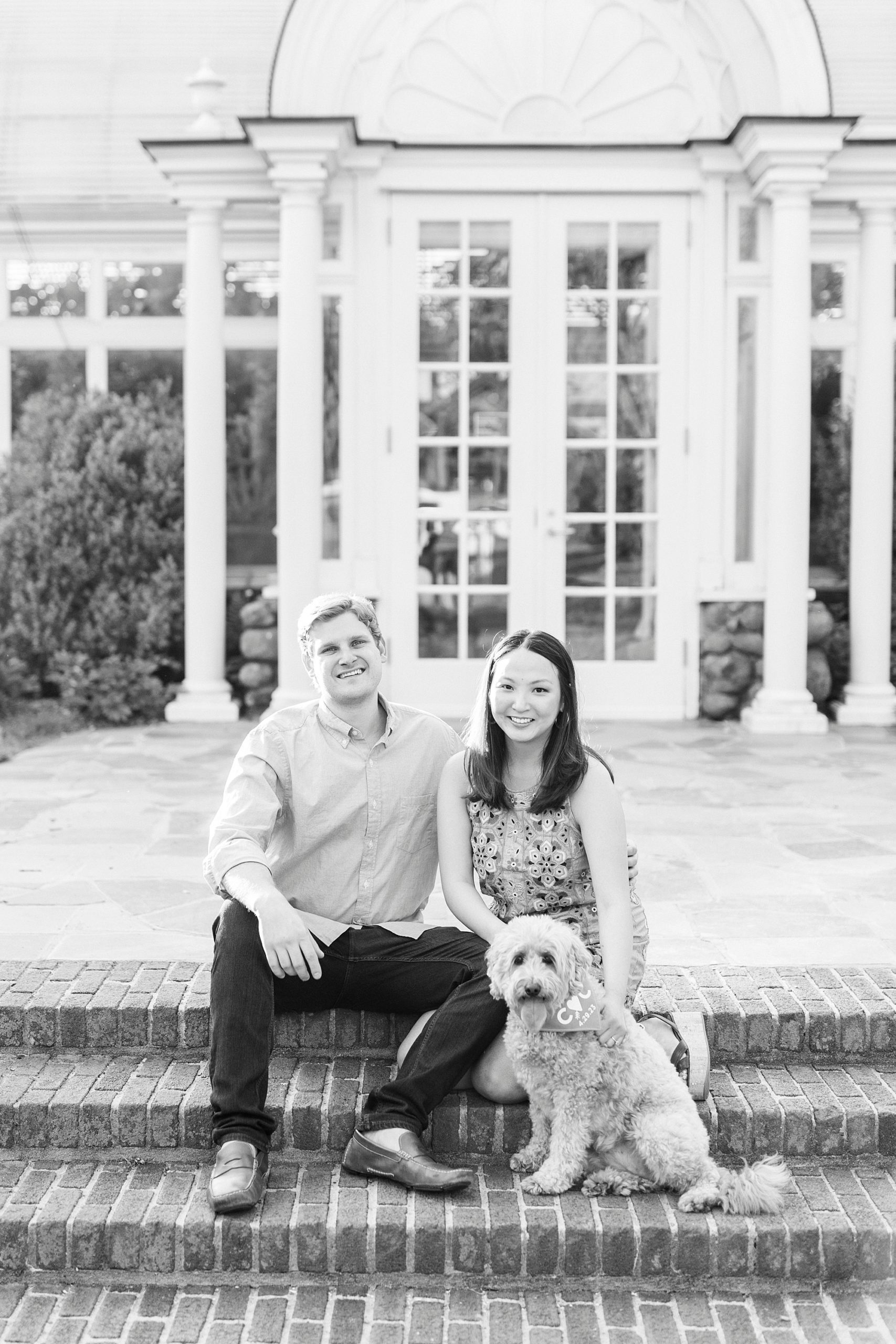 engaged couple sits together with dog sitting on brick steps at Reynolda Gardens