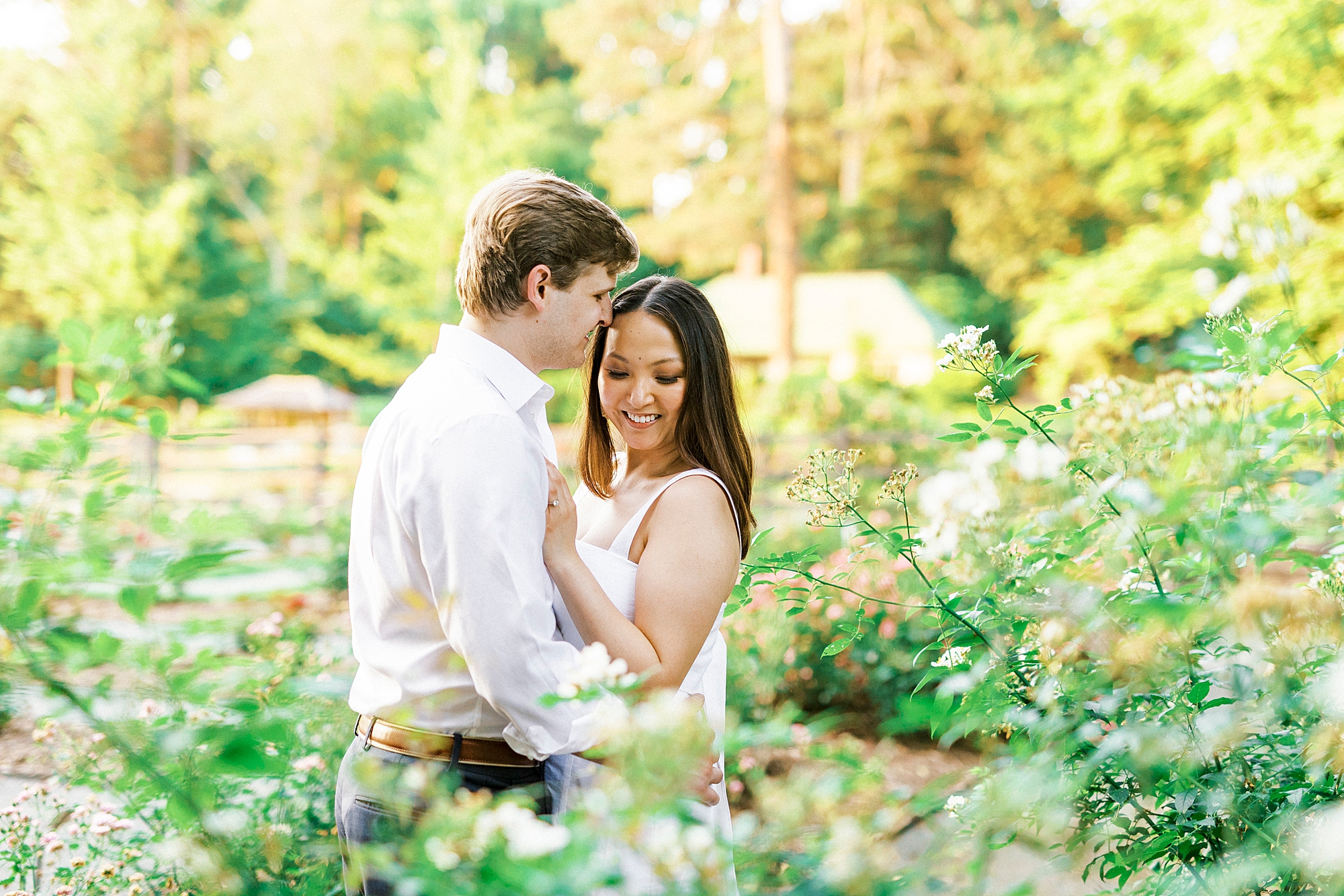 groom leans to kiss bride's forehead standing in gardens at Reynolda Gardens
