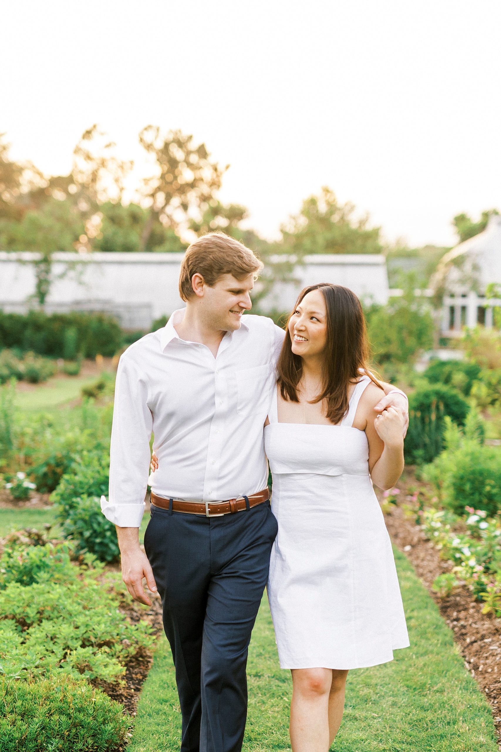 man in white button down shirt walks with woman in white summer dress through vines at Reynolda Gardens
