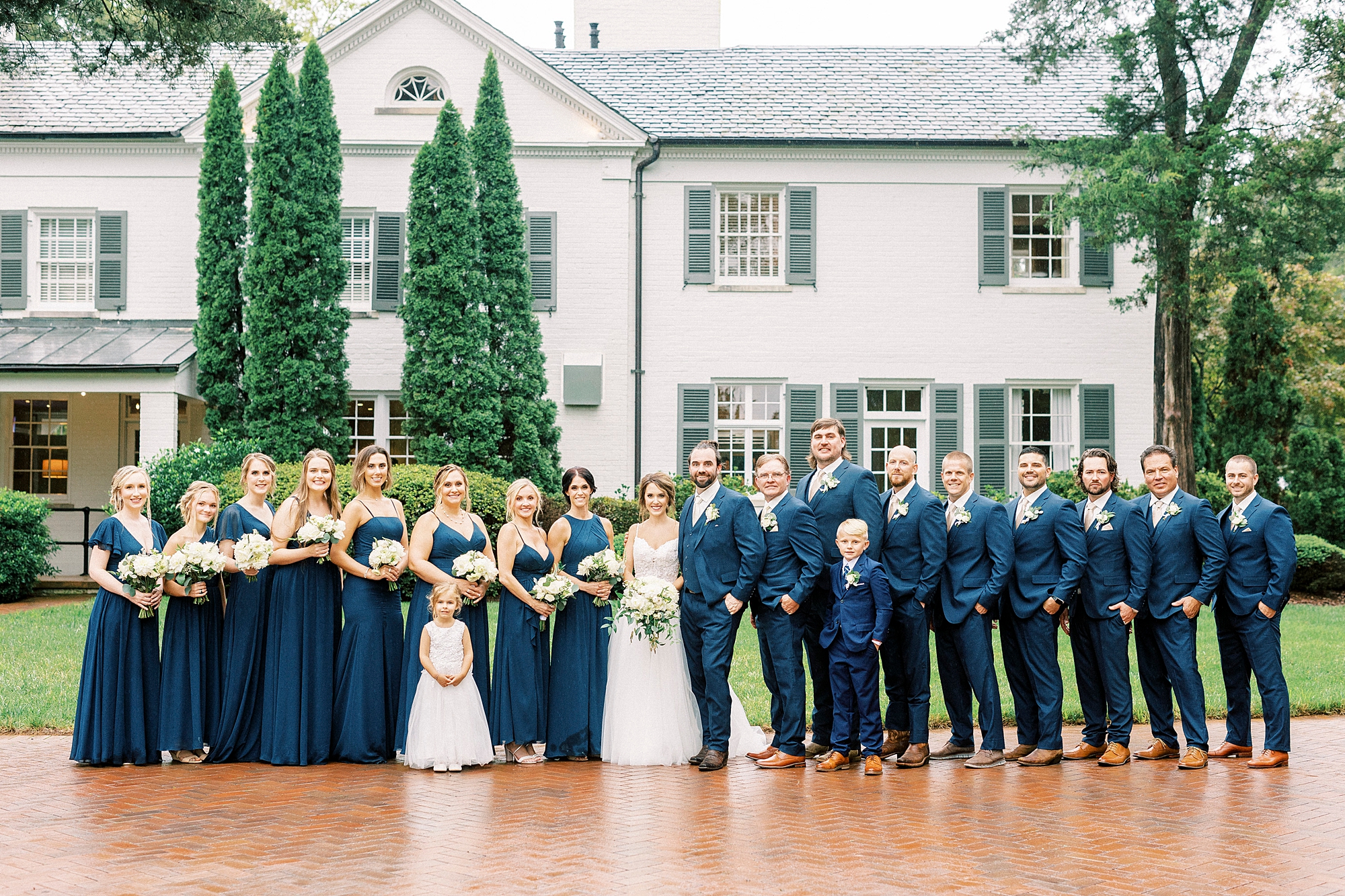 bride and groom stand with wedding party in navy dresses and navy suits