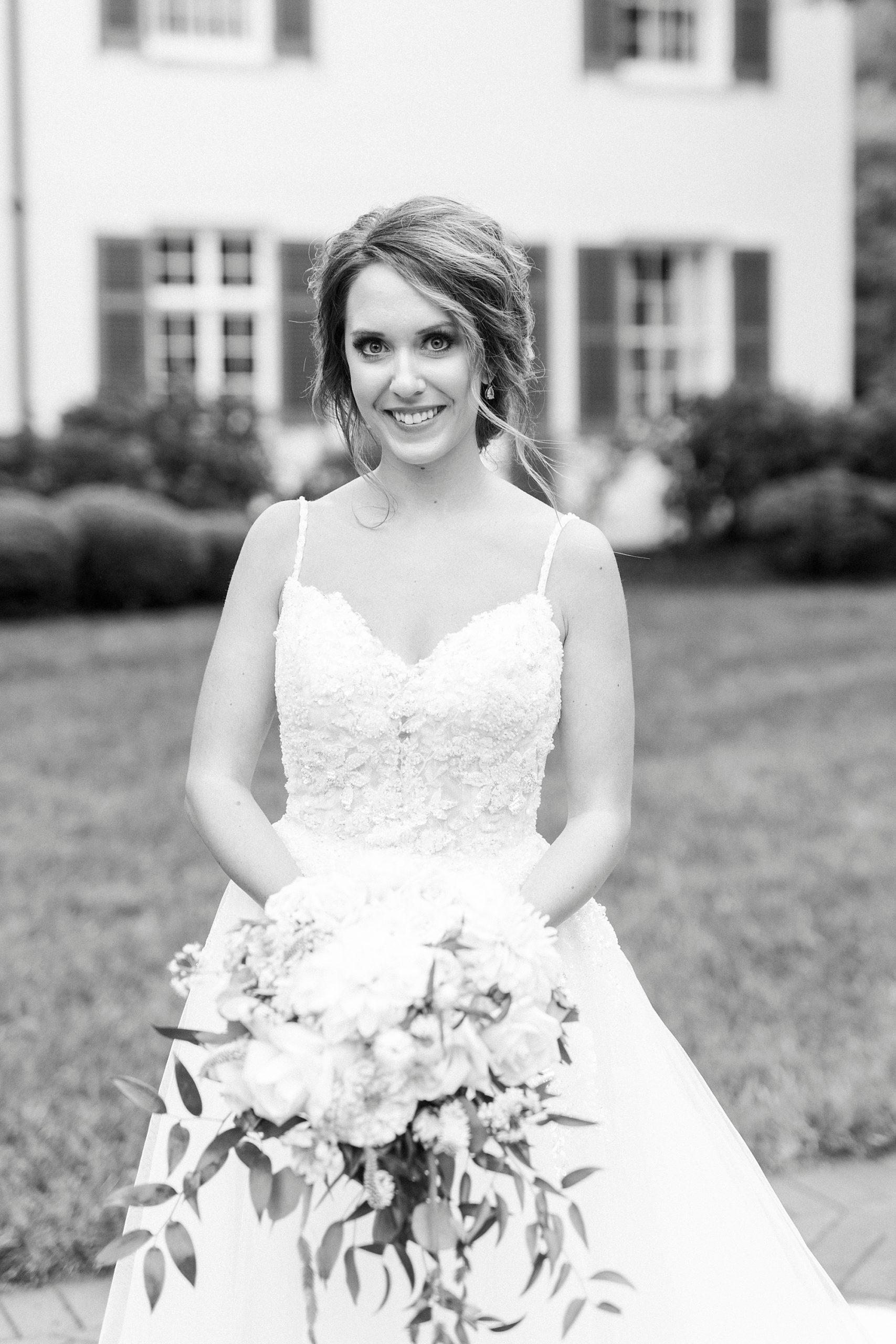 black and white portrait of bride standing on lawn in wedding gown