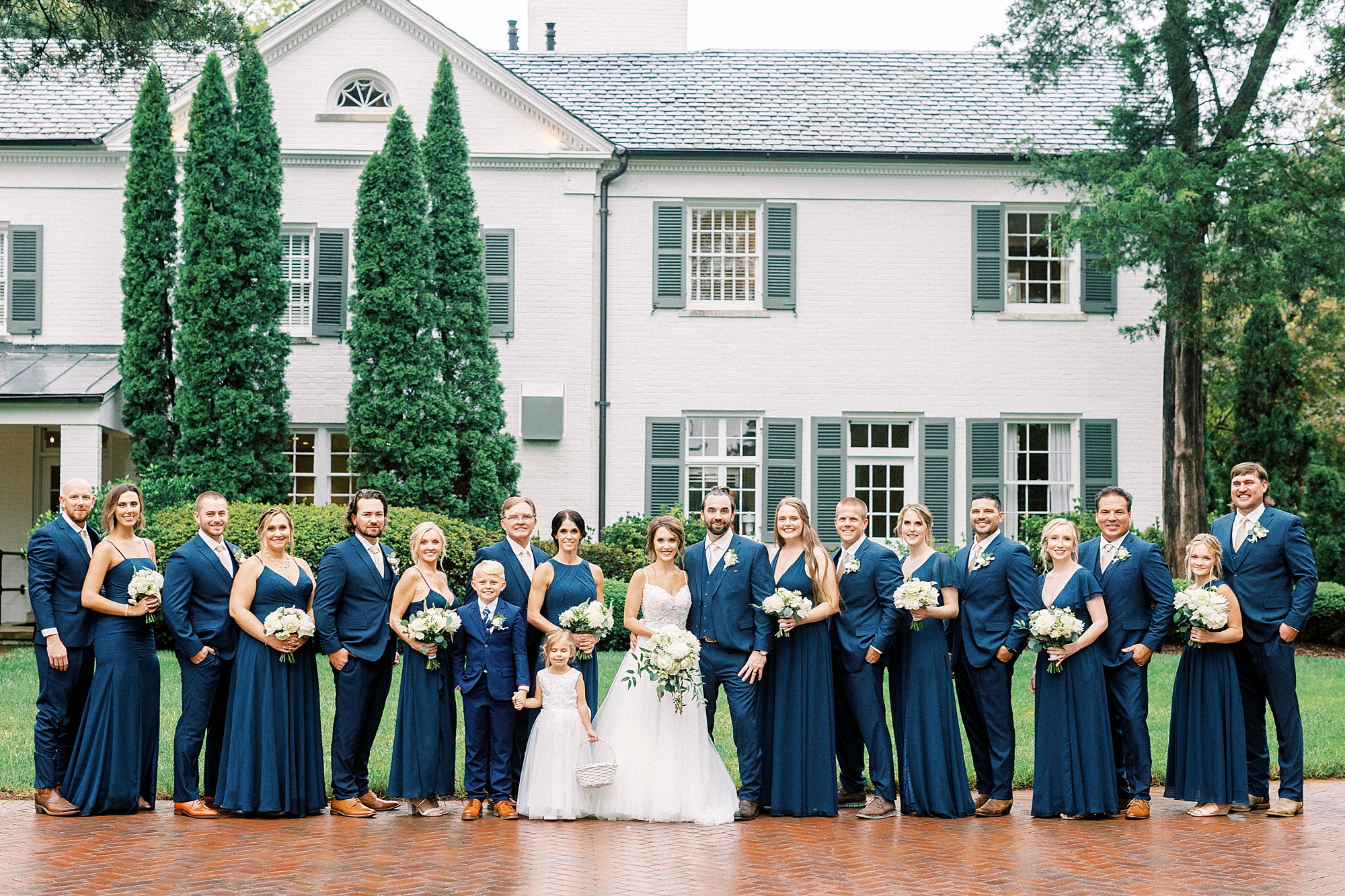 newlyweds stand with wedding party in navy dresses and suits outside Boxwood Estate