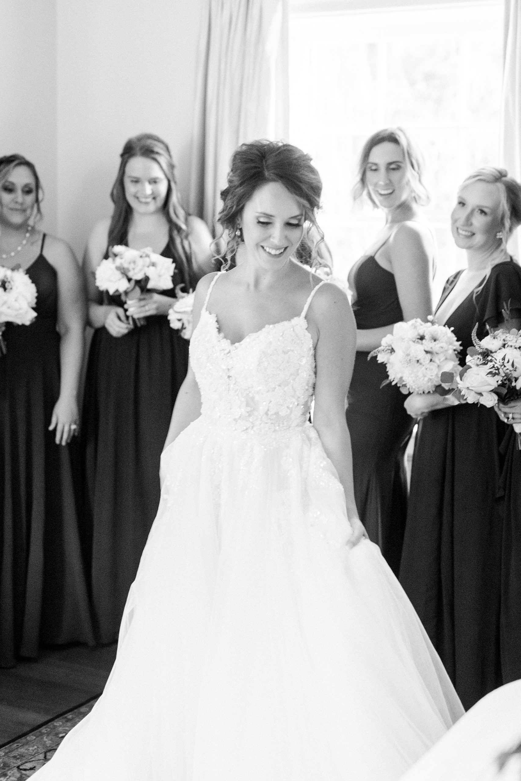 bridesmaids in dark gowns smile at bride during first look