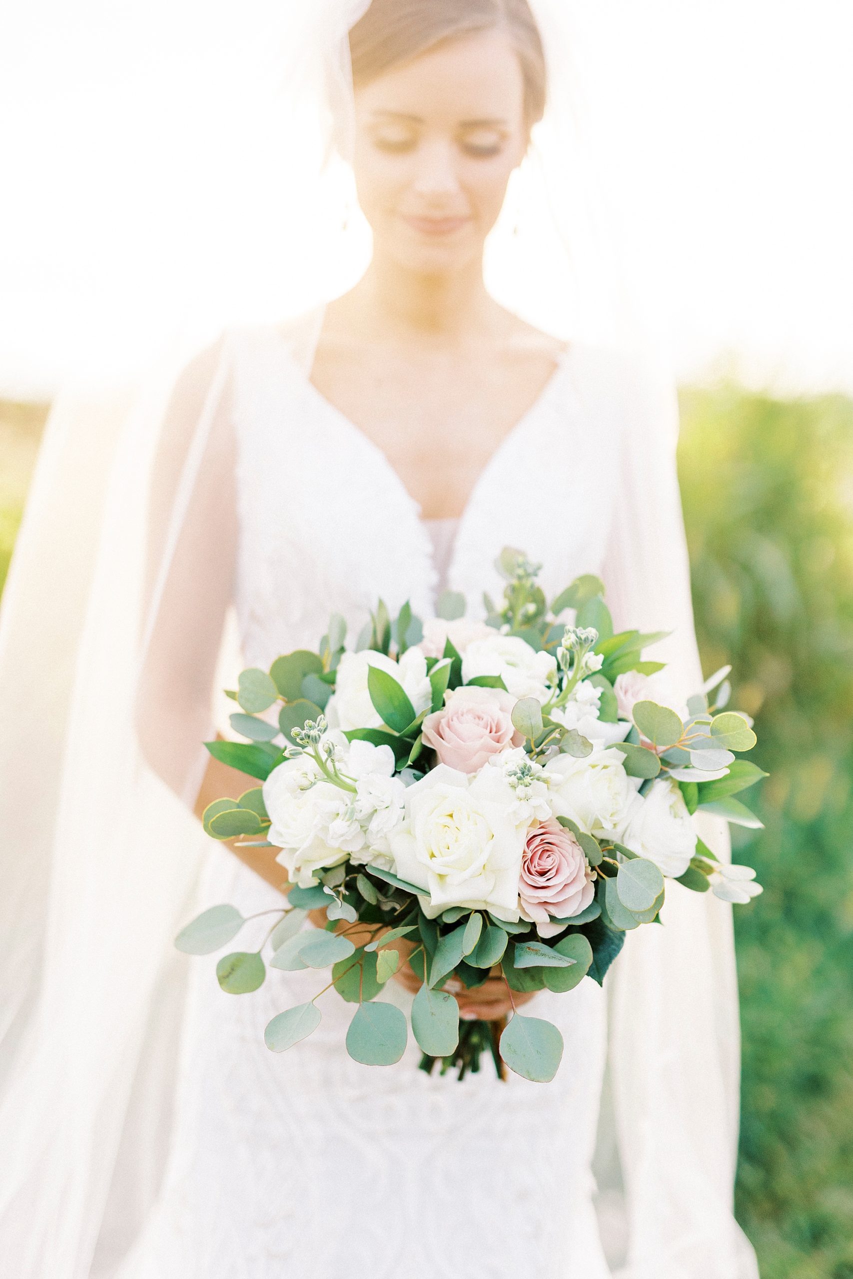 bride stands holding bouquet of white and pink flowers with veil behind her 