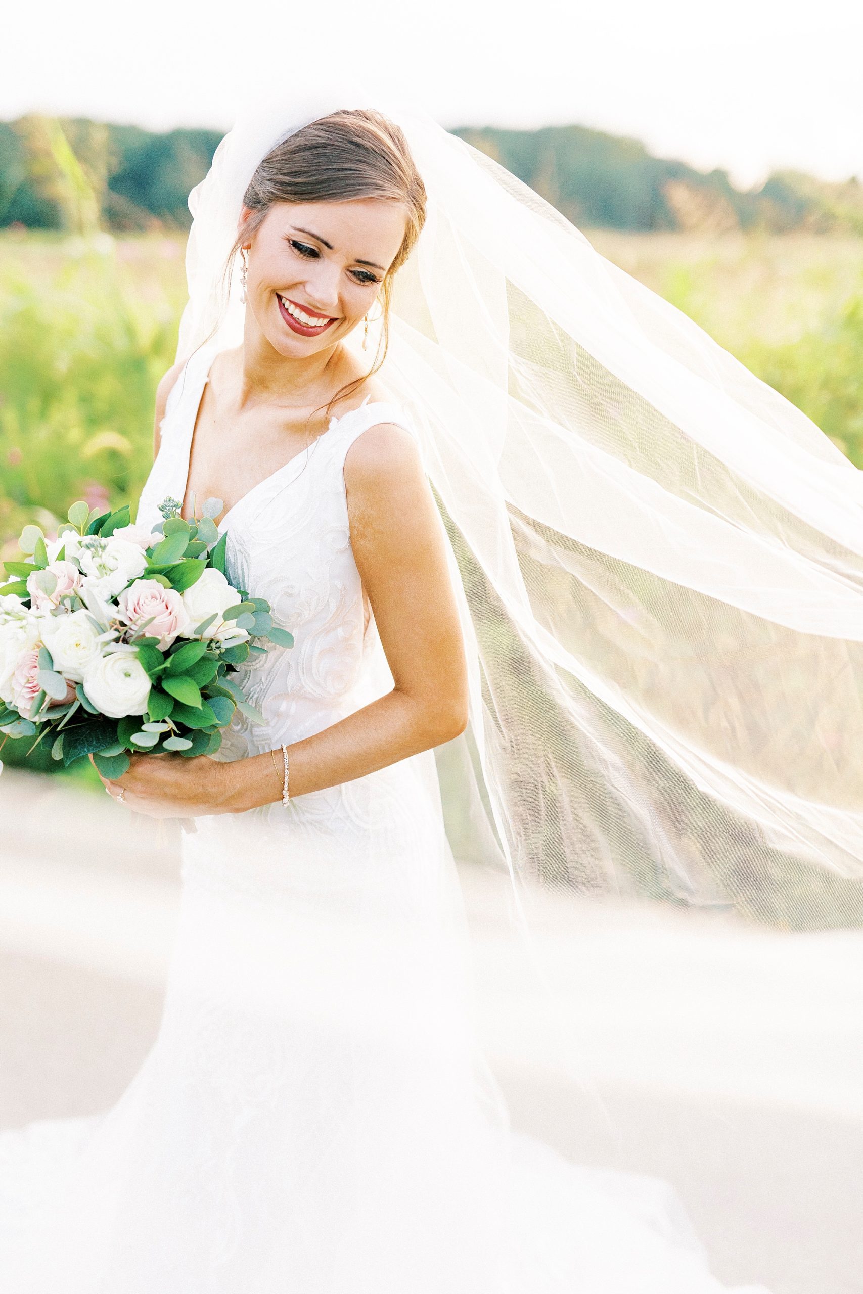 bride smiles down over shoulder while veil drapes around her 